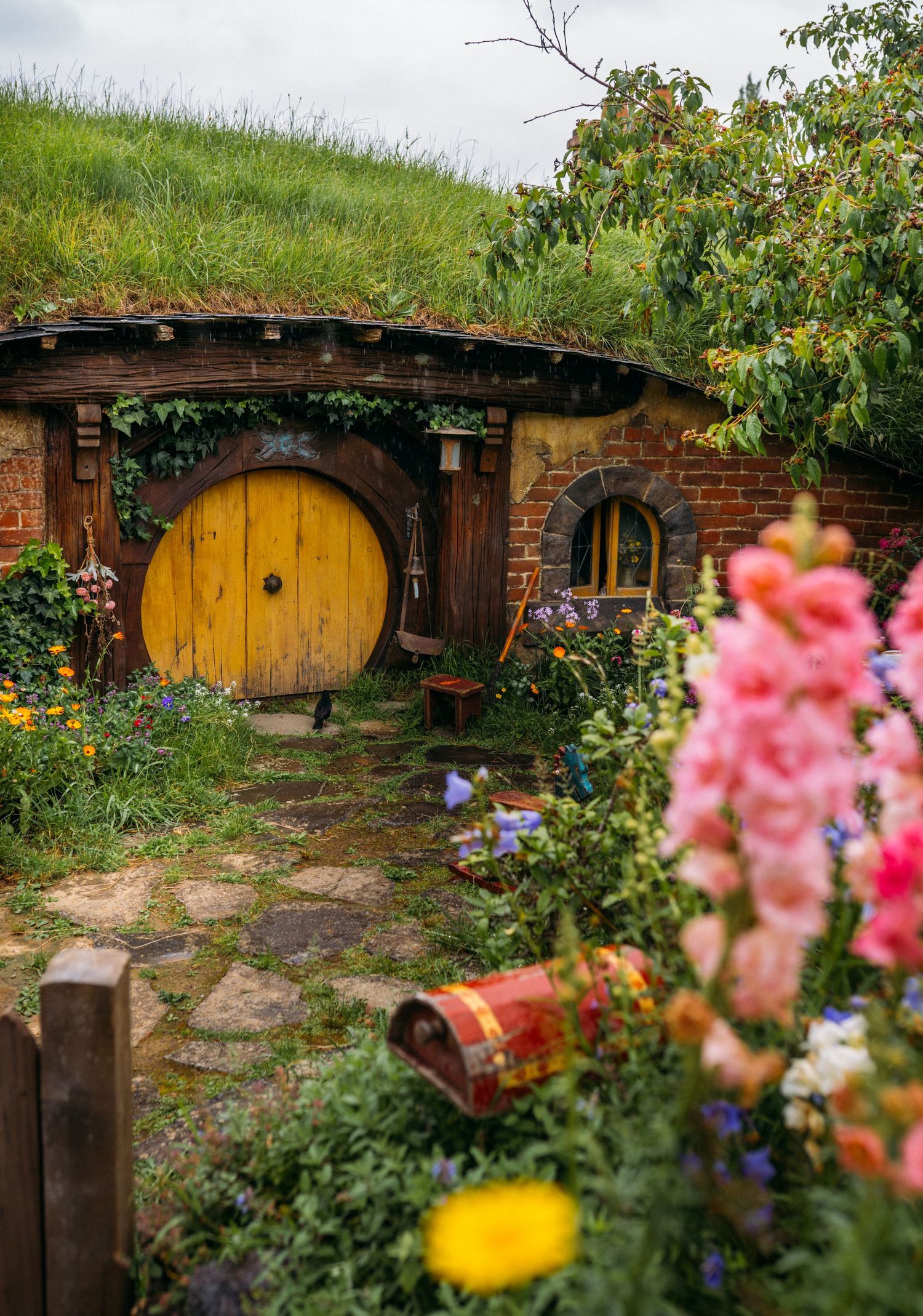 Charming Hobbiton movie set hobbit hole with yellow round door surrounded by colorful garden flowers.