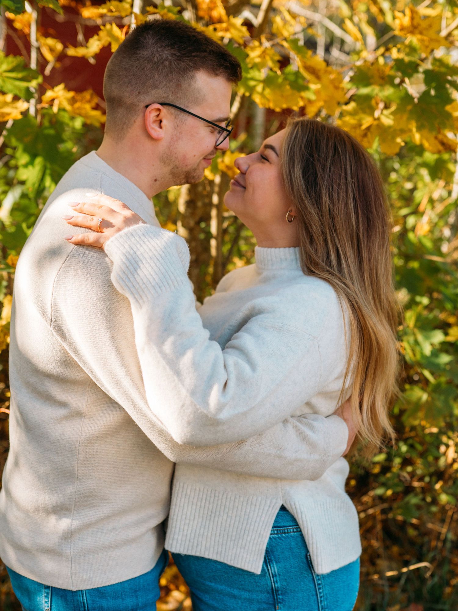 Couple in matching cream sweaters and jeans sharing a romantic moment surrounded by golden autumn foliage.
