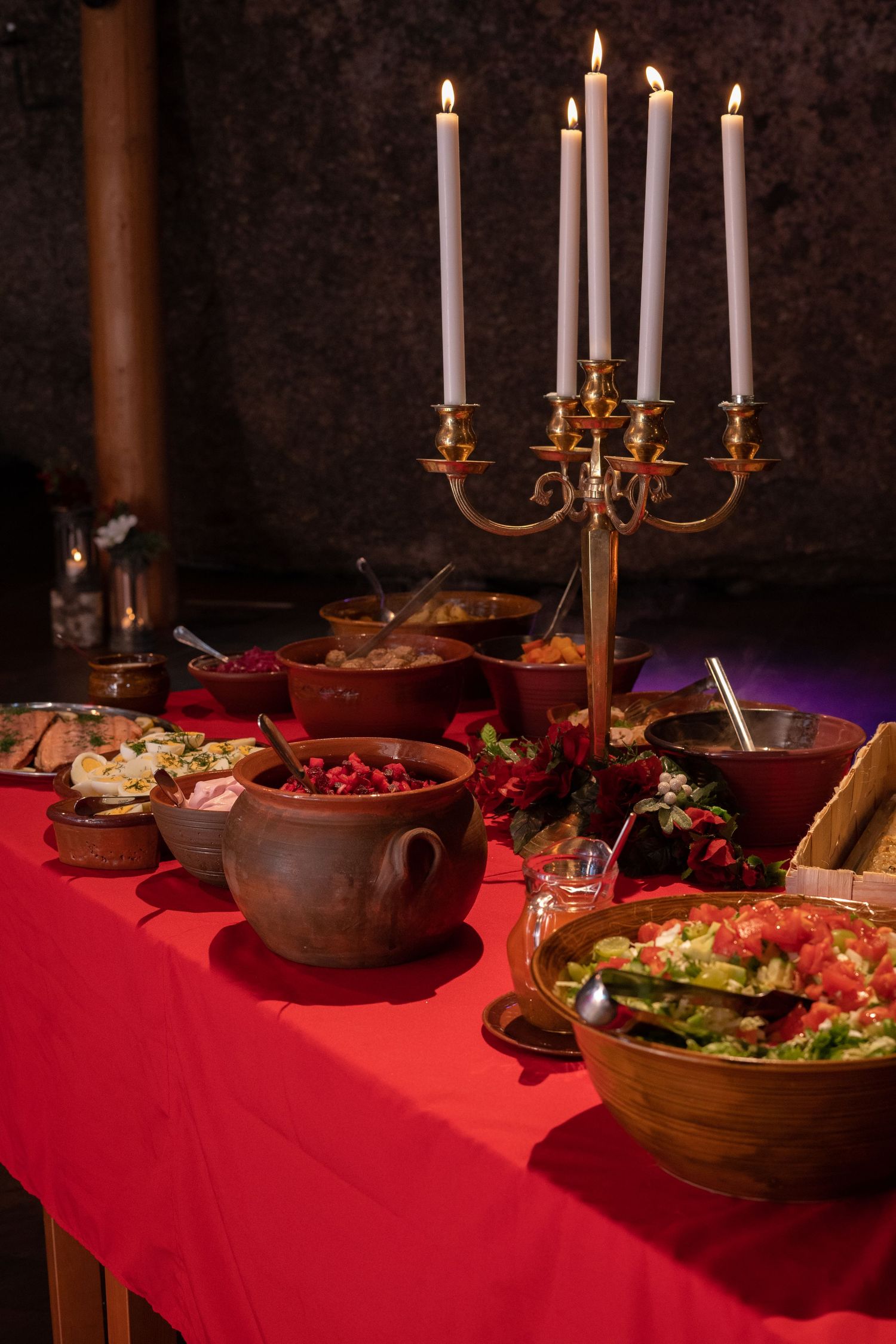 Festive dinner table with red cloth, candelabra, and assorted dishes including salads and soups.