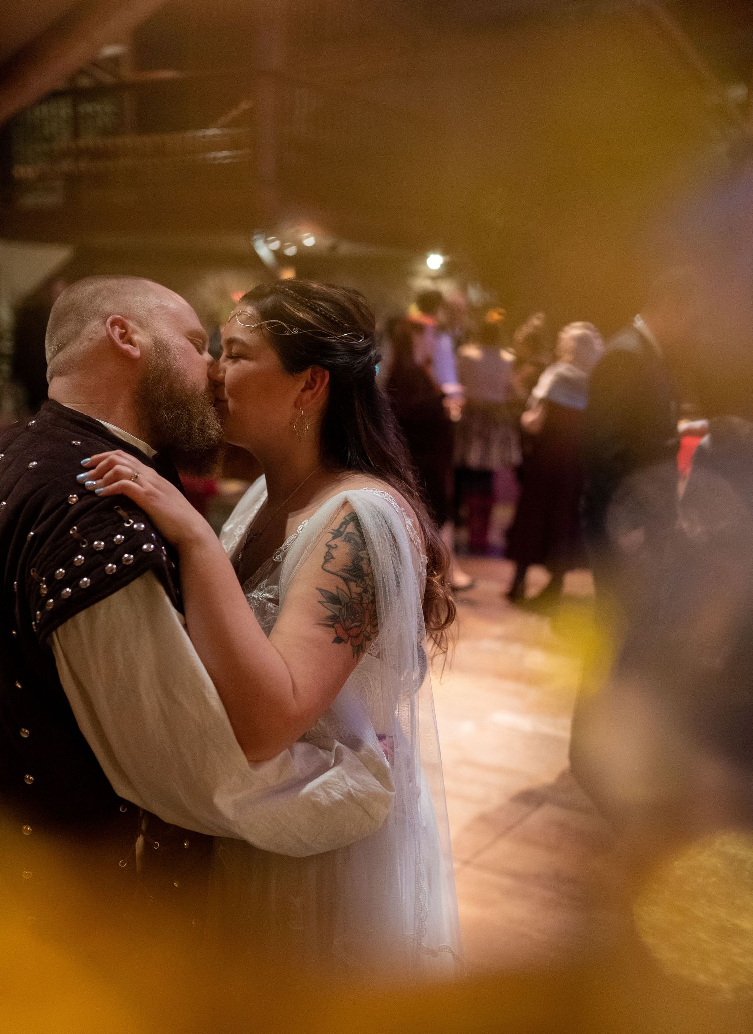Bride and groom sharing romantic kiss on wedding dance floor with warm golden lighting.