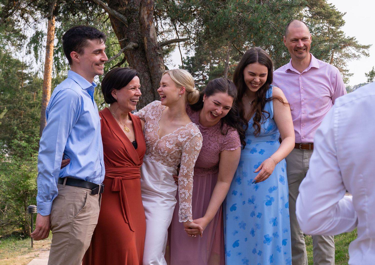 Group of six wedding guests laughing and celebrating together outdoors at a summer wedding reception.