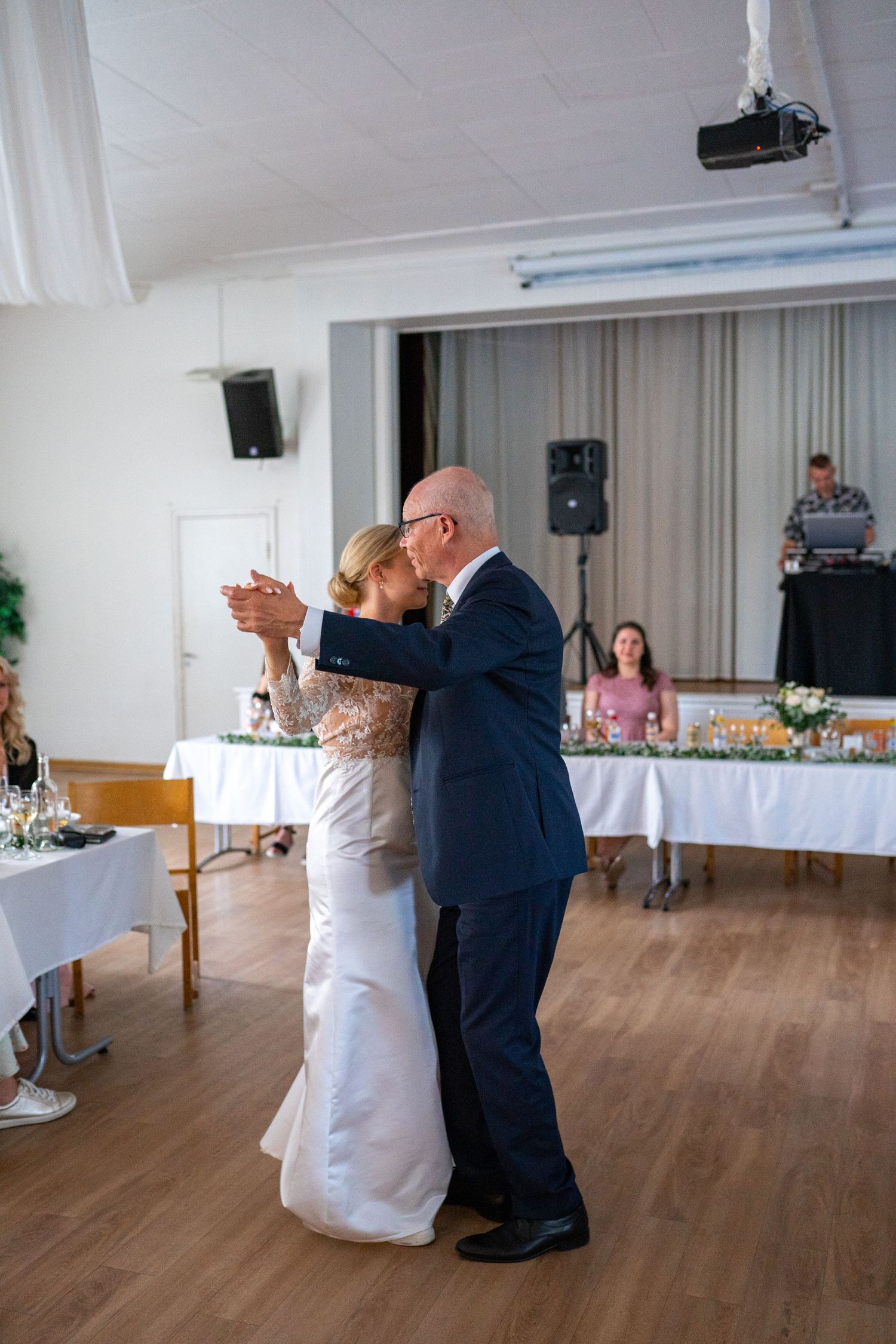 Bride dances with older gentleman in navy suit at wedding reception, likely father-daughter dance.