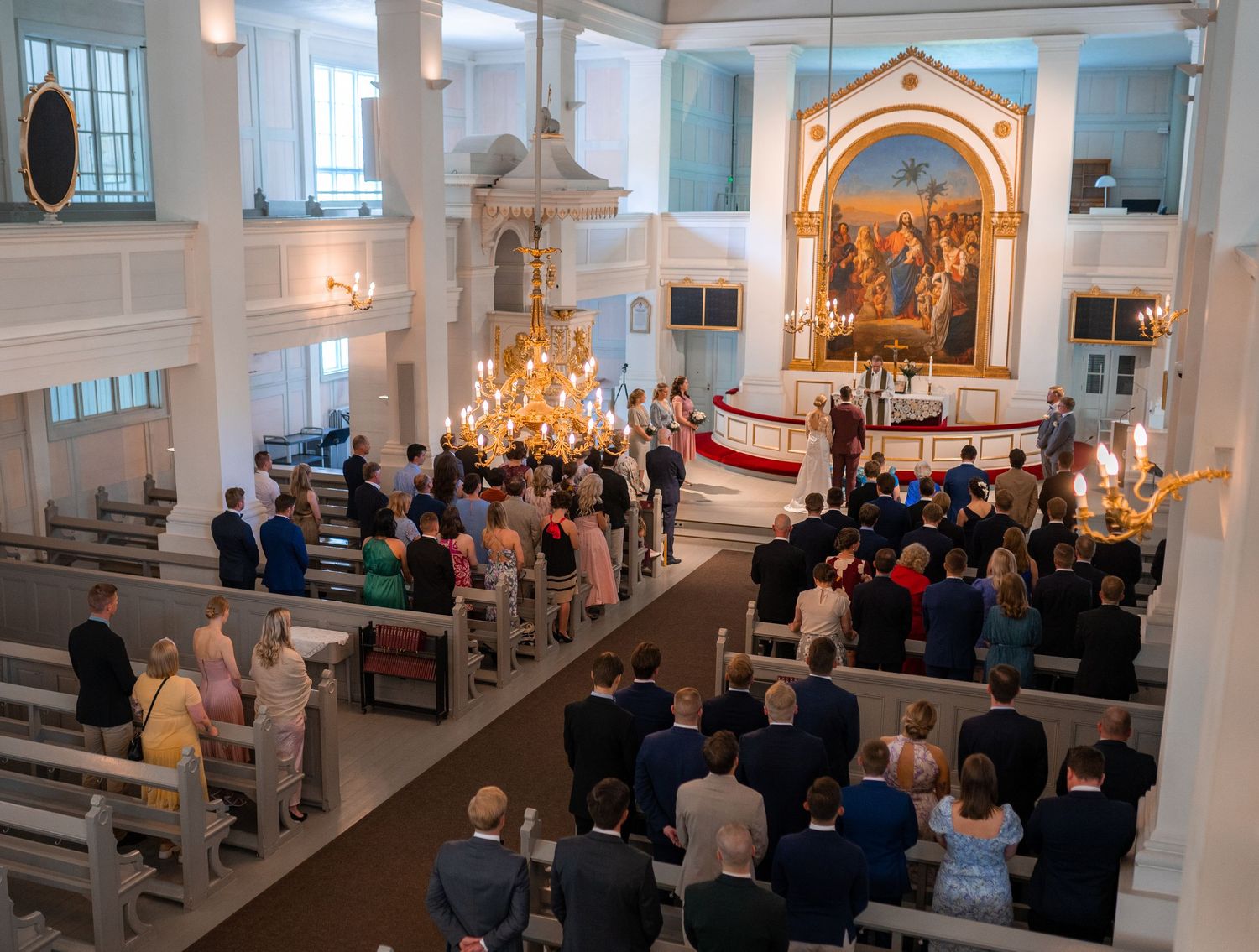Overhead view of packed church wedding ceremony with guests in pews and couple at the ornate golden altar.