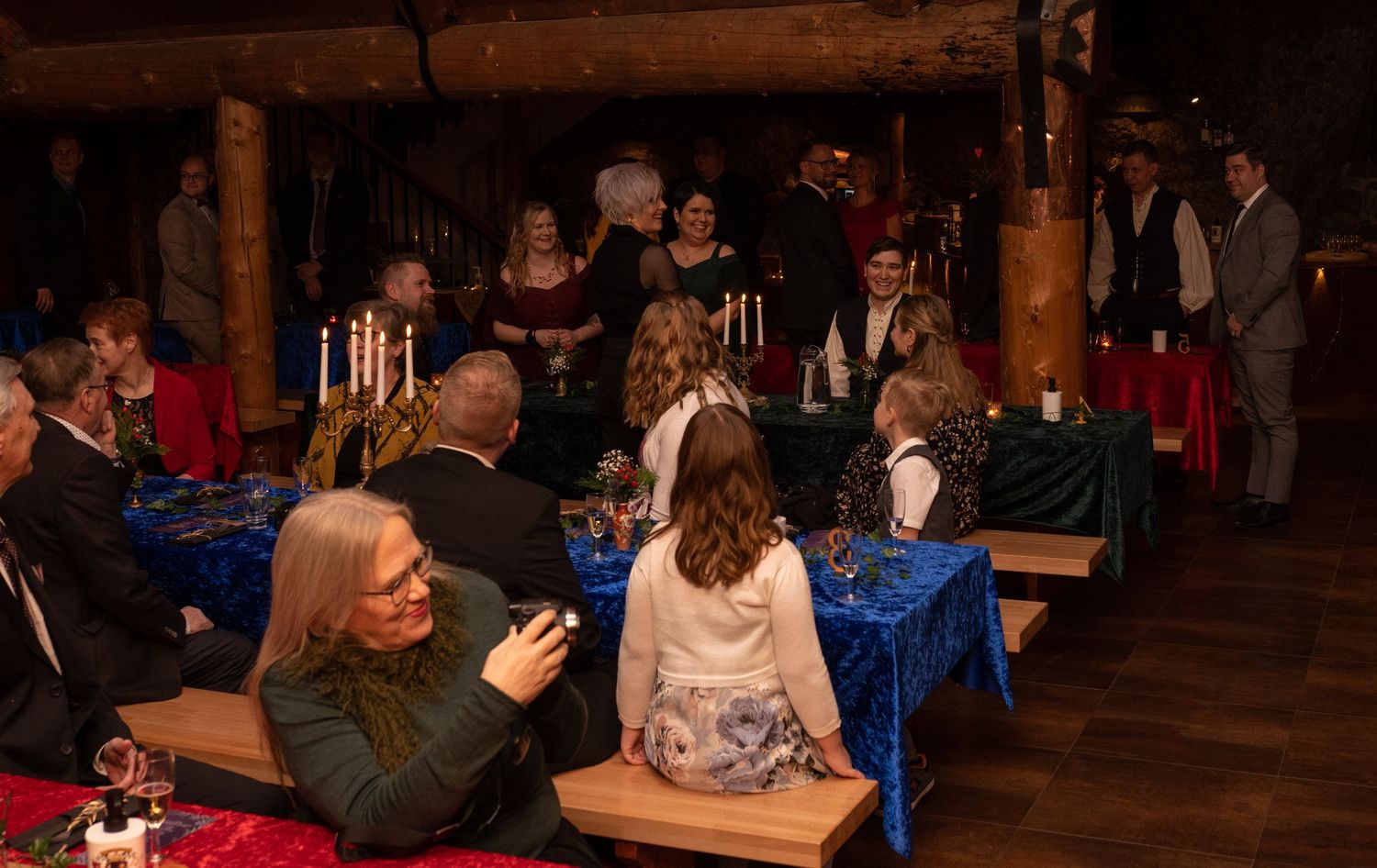 Guests gather at a medieval-themed banquet hall with candlelit blue tables during a festive evening event.