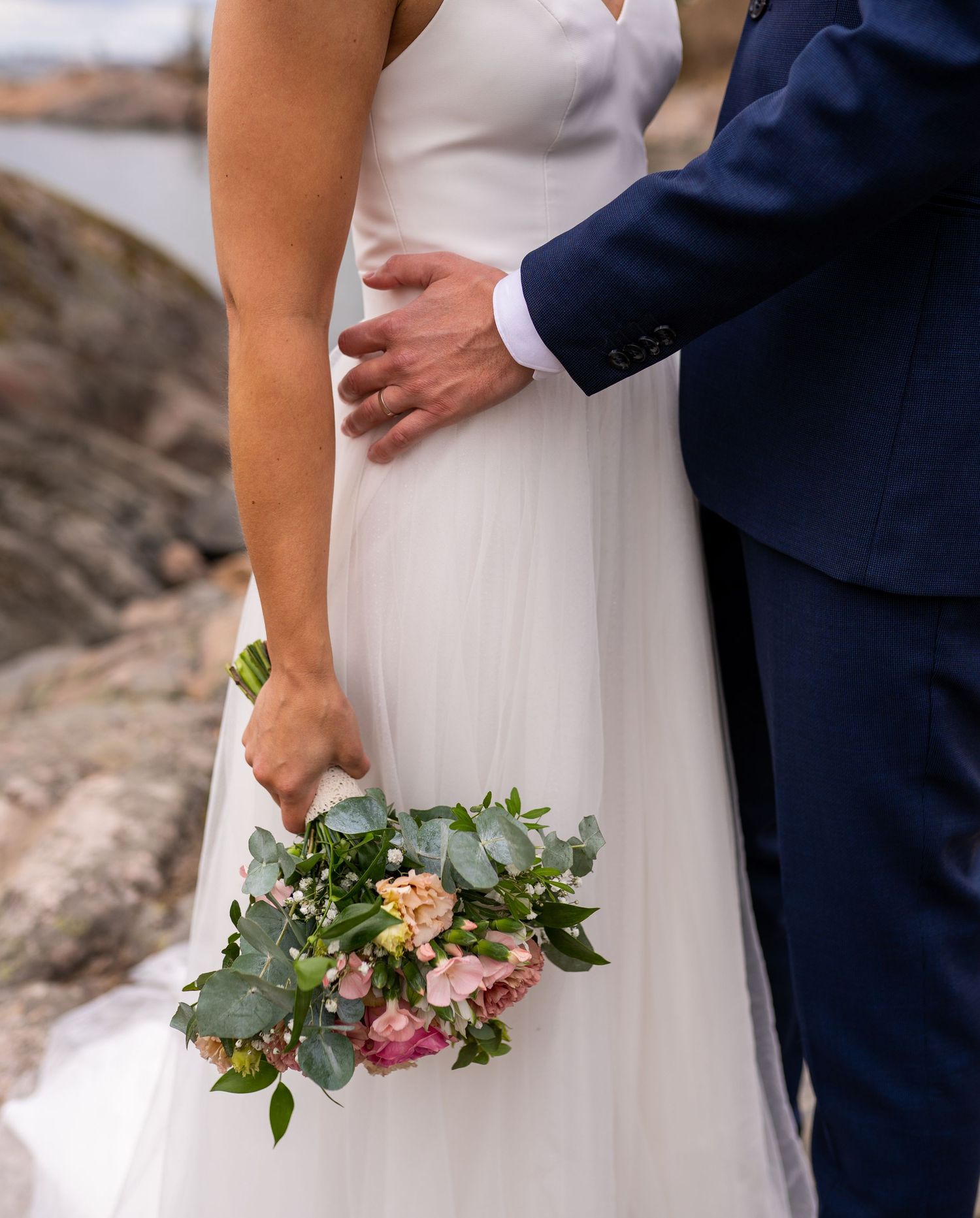 Close-up of bride holding a pink floral bouquet with groom's hand on her waist.