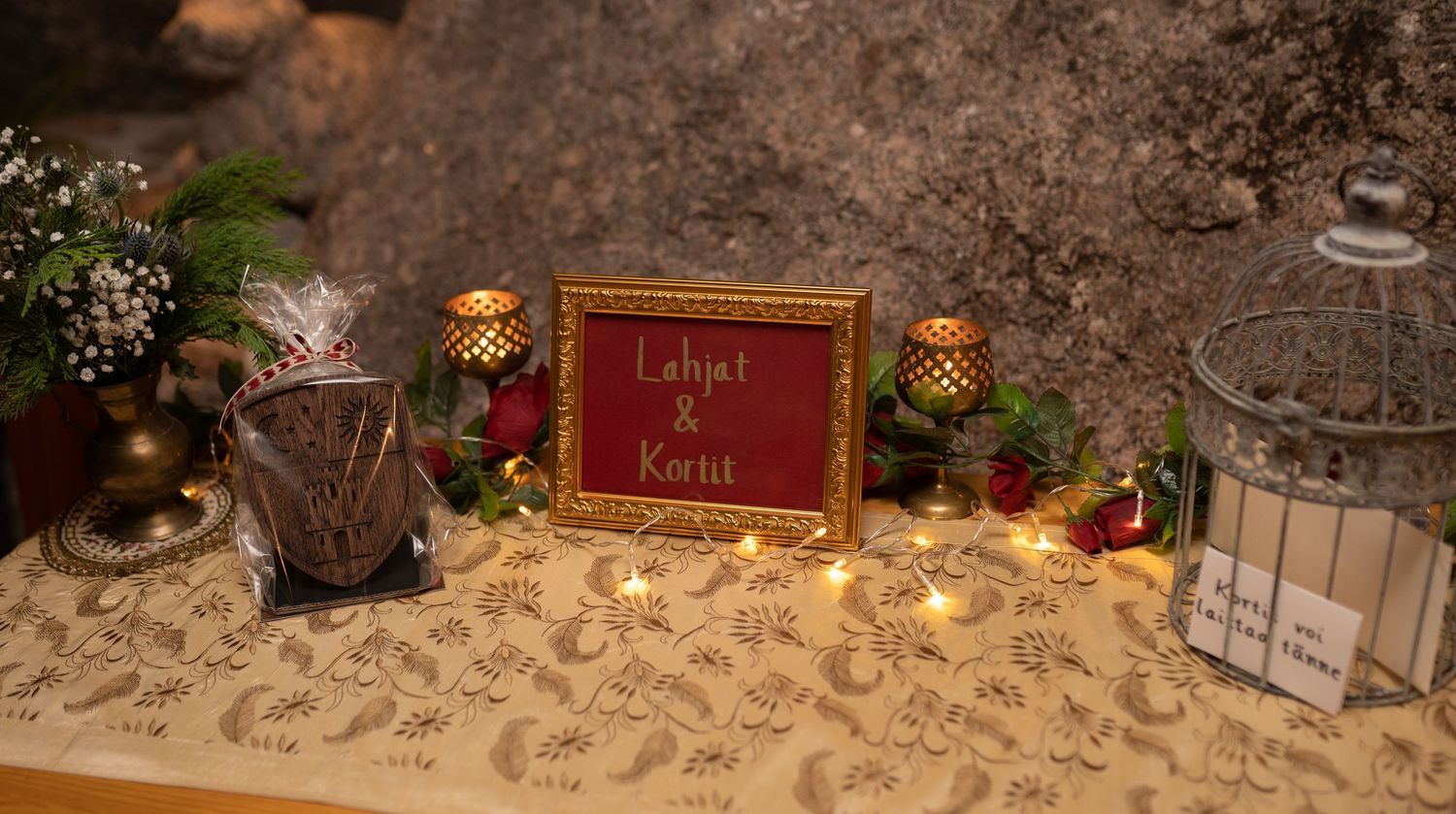 Elegant wedding gift table with candles, greenery, and a red framed sign reading Lahjat & Kortit.
