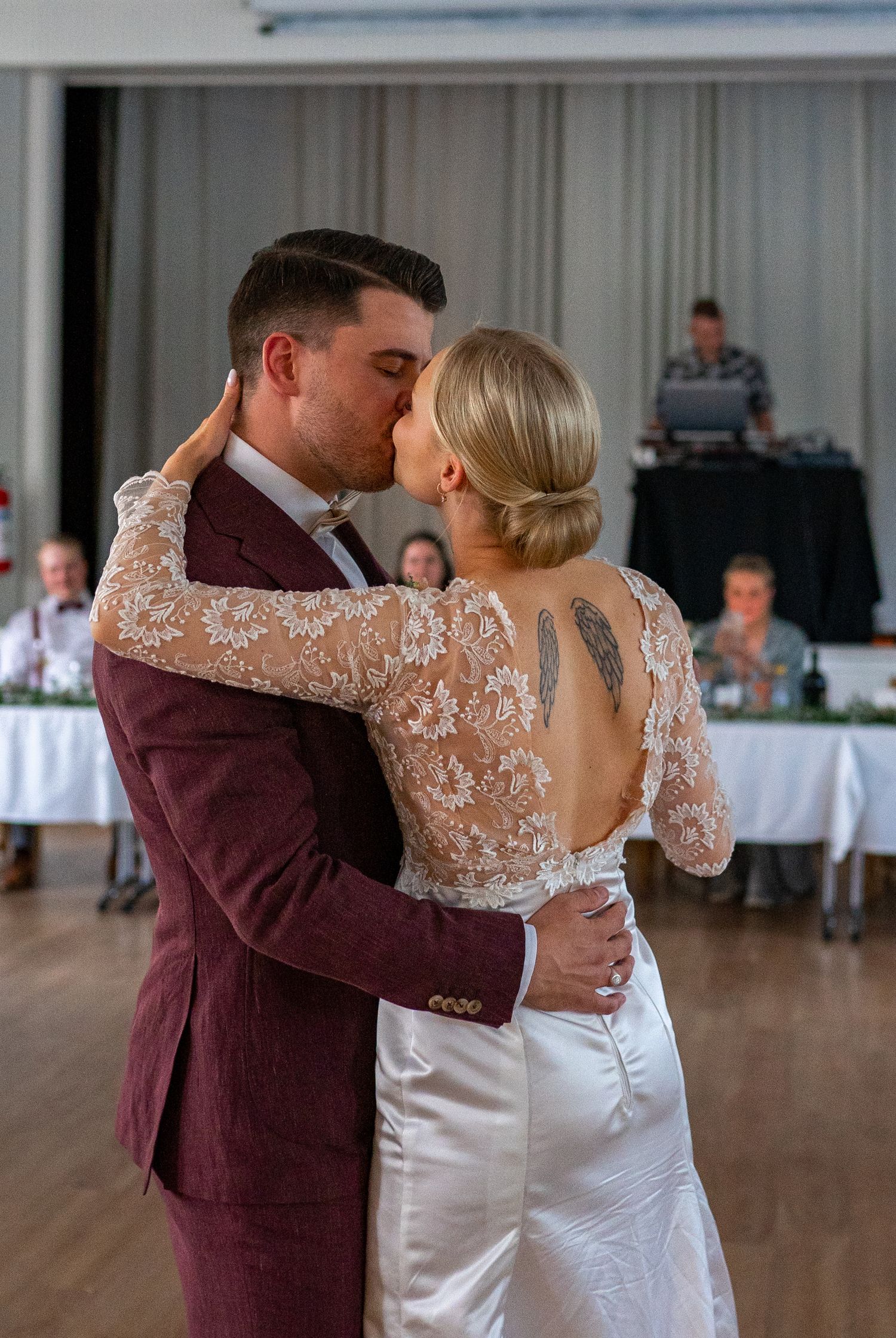Bride and groom share a romantic kiss during first dance, bride wearing lace gown with back tattoo.