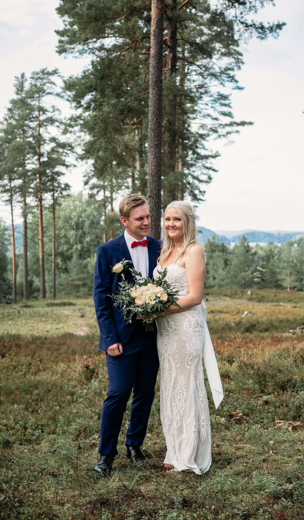 Smiling bride and groom pose together in a scenic pine forest during their wedding day.