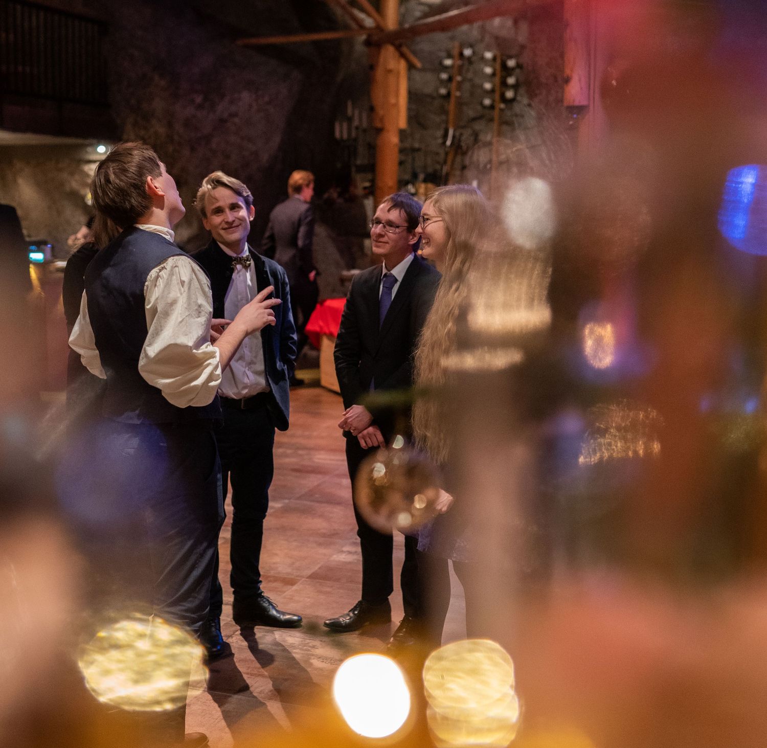 Group of elegantly dressed people socializing at an upscale indoor evening event with warm ambient lighting.