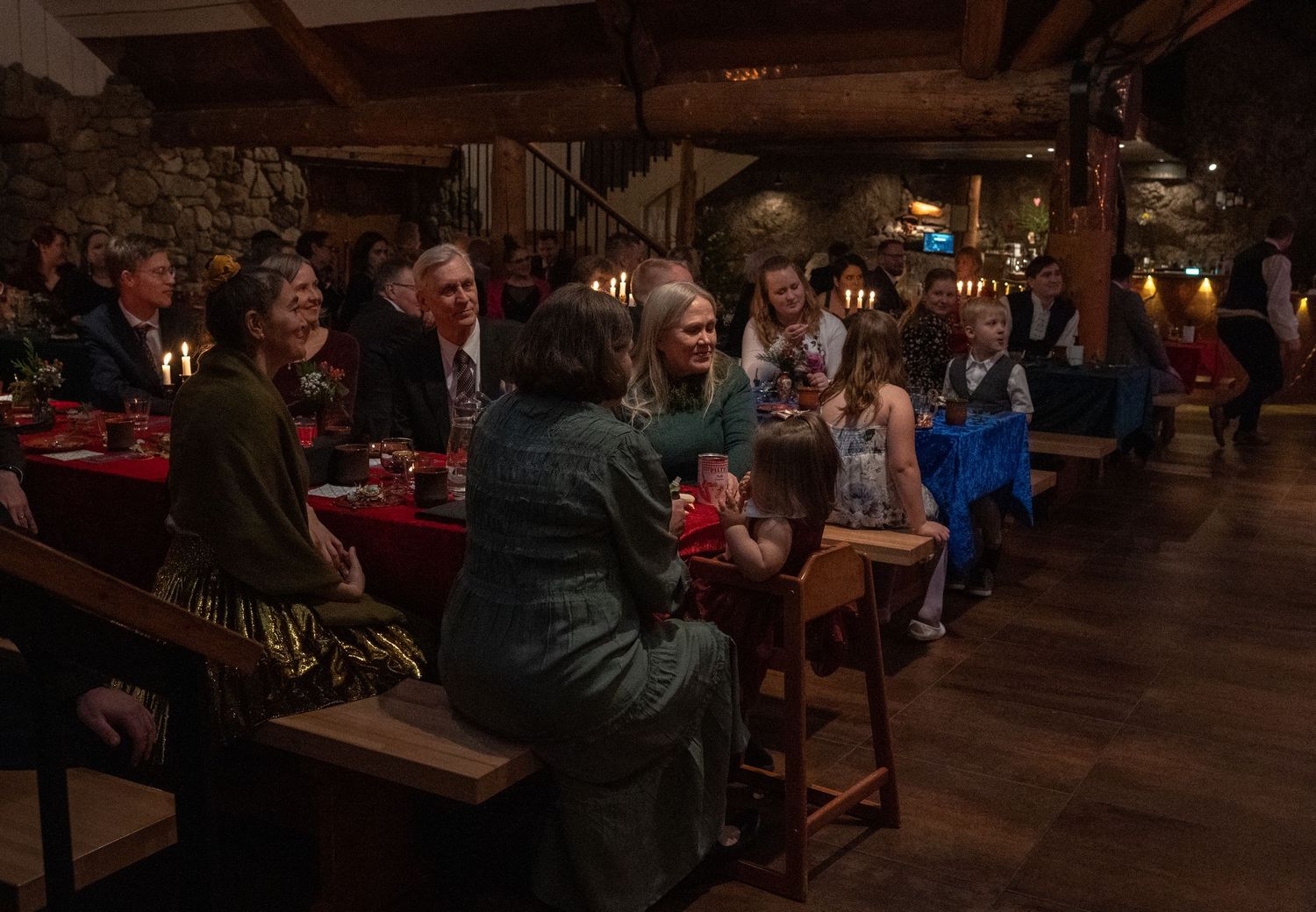 Guests gathered at a candlelit rustic restaurant with stone walls, enjoying a festive dinner party together.