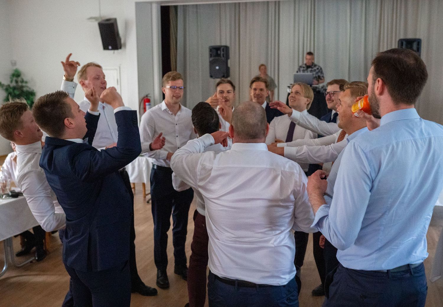 Groomsmen and male wedding guests gather in a circle celebrating together on the dance floor.