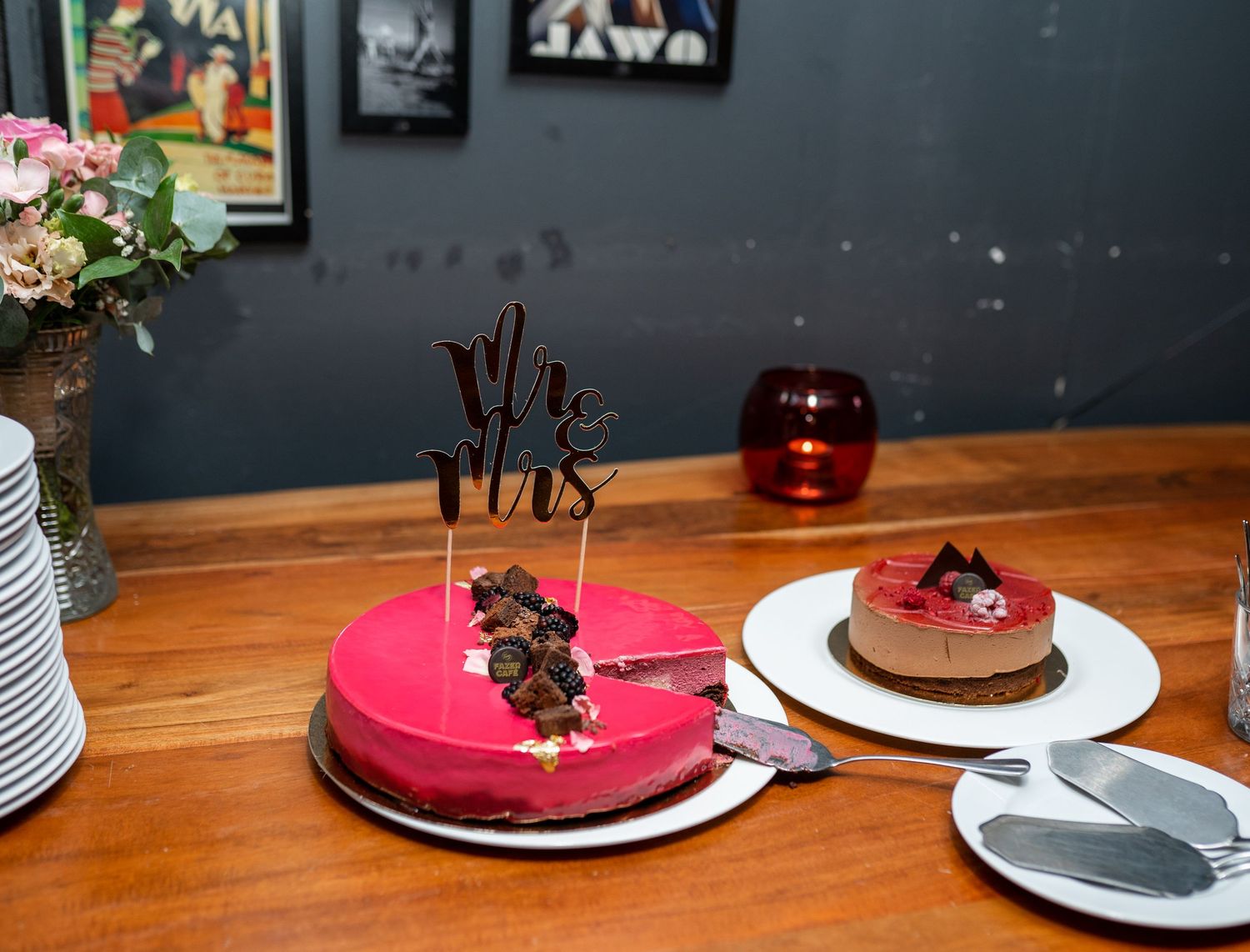 Elegant pink wedding cake with Mr and Mrs topper beside chocolate cake on wooden table.