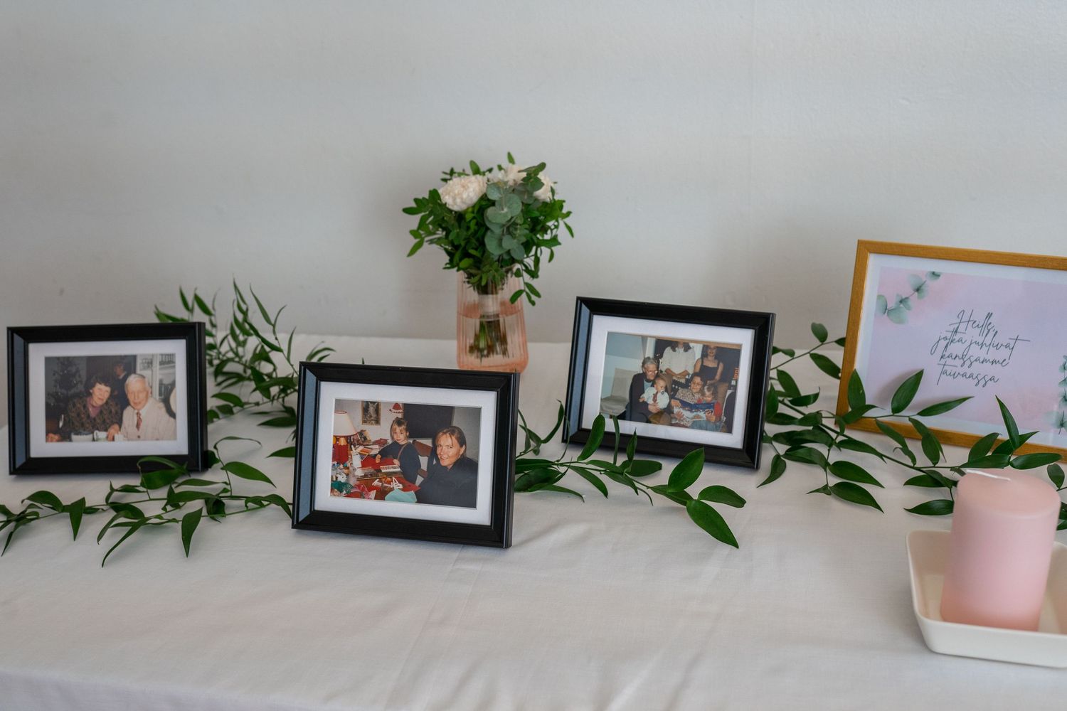 Wedding memory table with framed family photos, greenery garland, and floral arrangement.