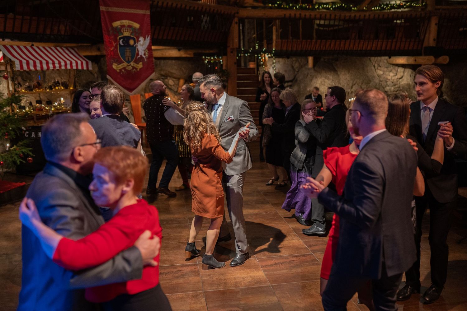 Couples dancing elegantly at a festive indoor event with warm lighting and medieval-style decor.