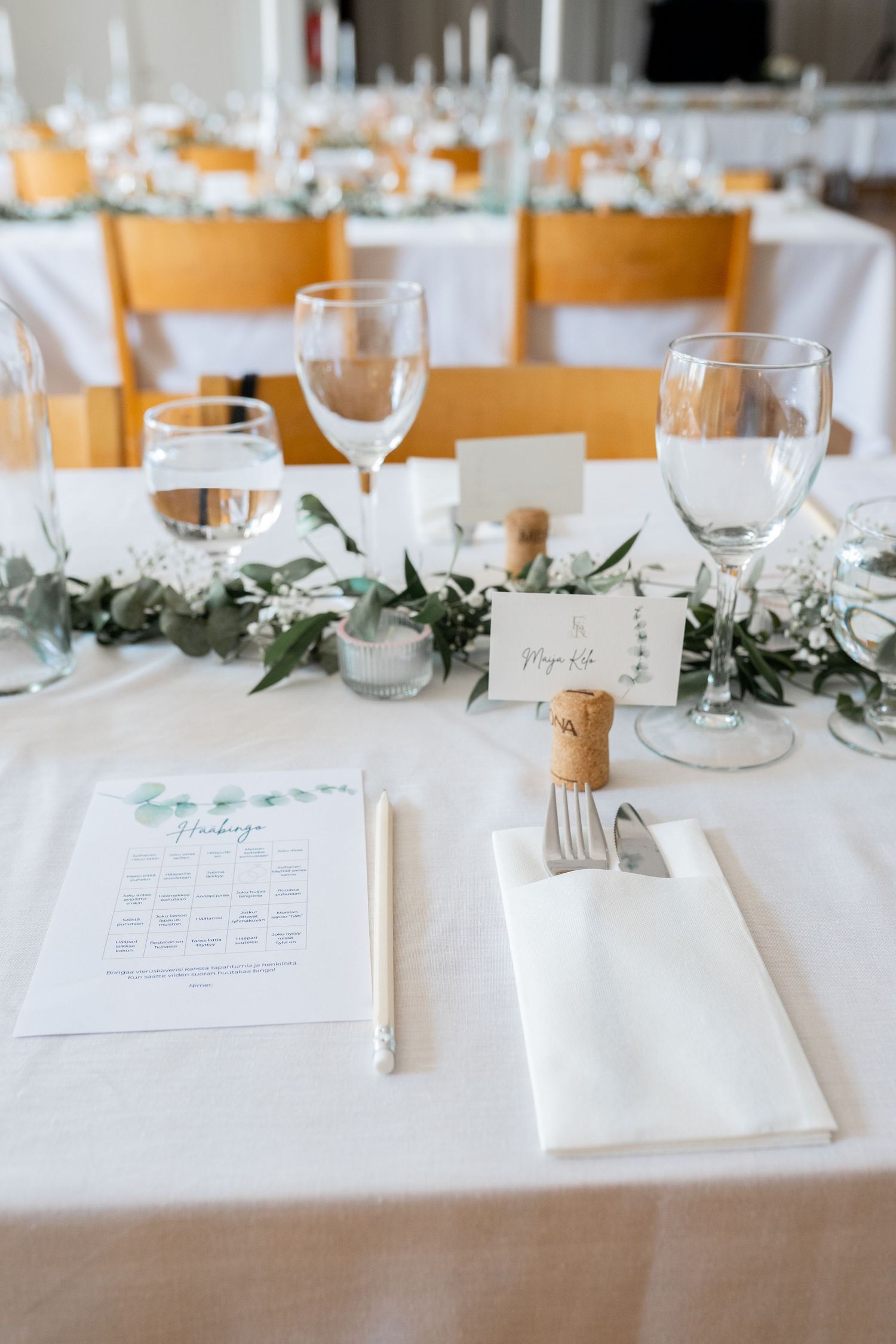Elegant wedding table setting with white linens, greenery garland, and place cards.