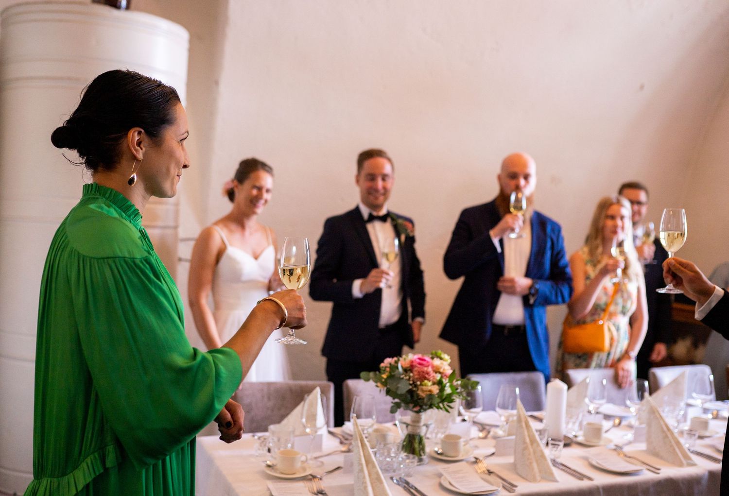 Woman in green dress toasting with champagne as wedding guests raise glasses at reception.