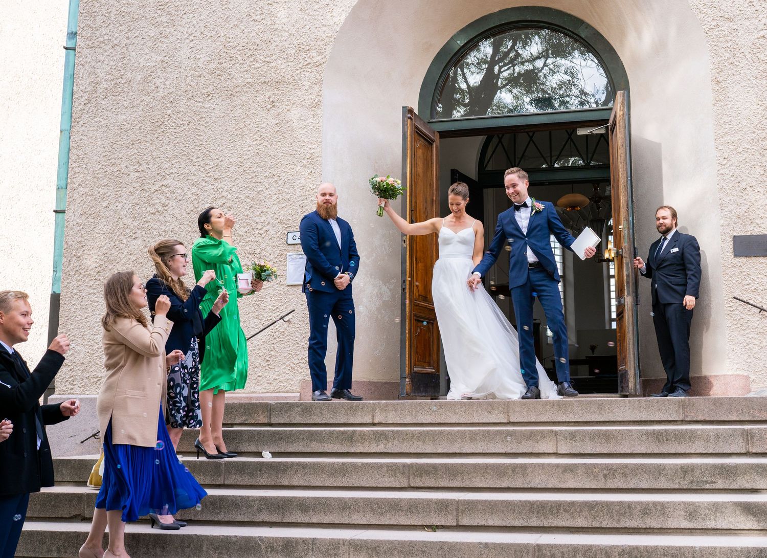 Bride tosses bouquet as newlyweds celebrate with guests on church steps.