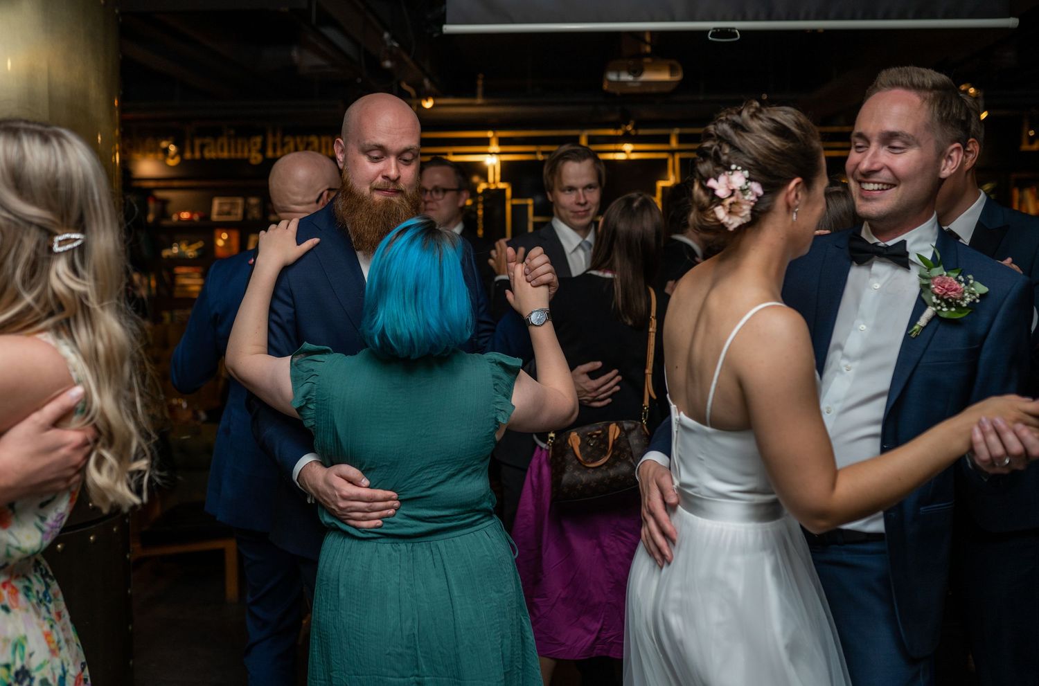 Wedding guests dancing together on the dance floor, including bride in white gown and man with blue hair.