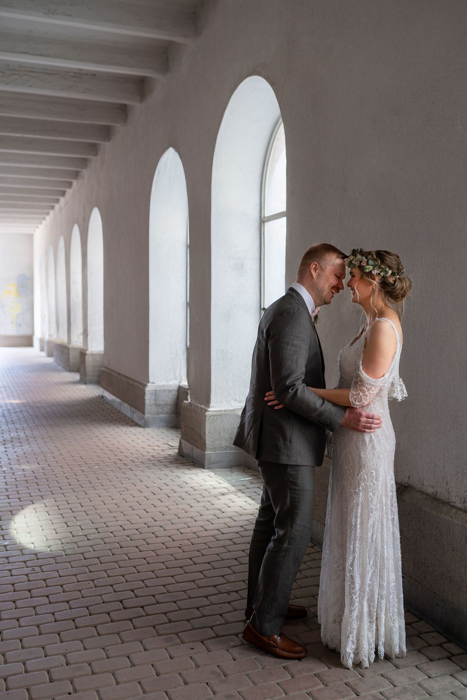 Bride and groom share a romantic moment in an elegant arched corridor on their wedding day.