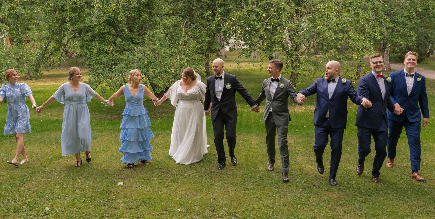 Wedding party joyfully runs holding hands across a green lawn in a fun outdoor group photo.