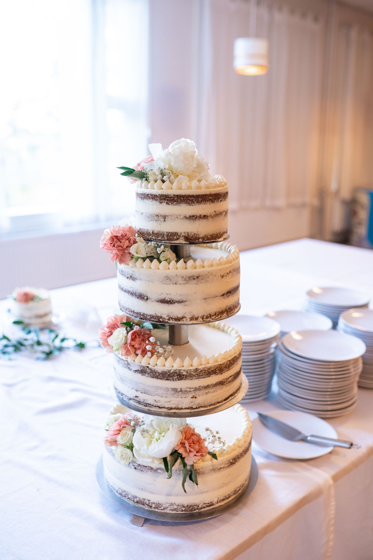 Elegant three-tier naked wedding cake decorated with fresh pink and white flowers on a white tablecloth.