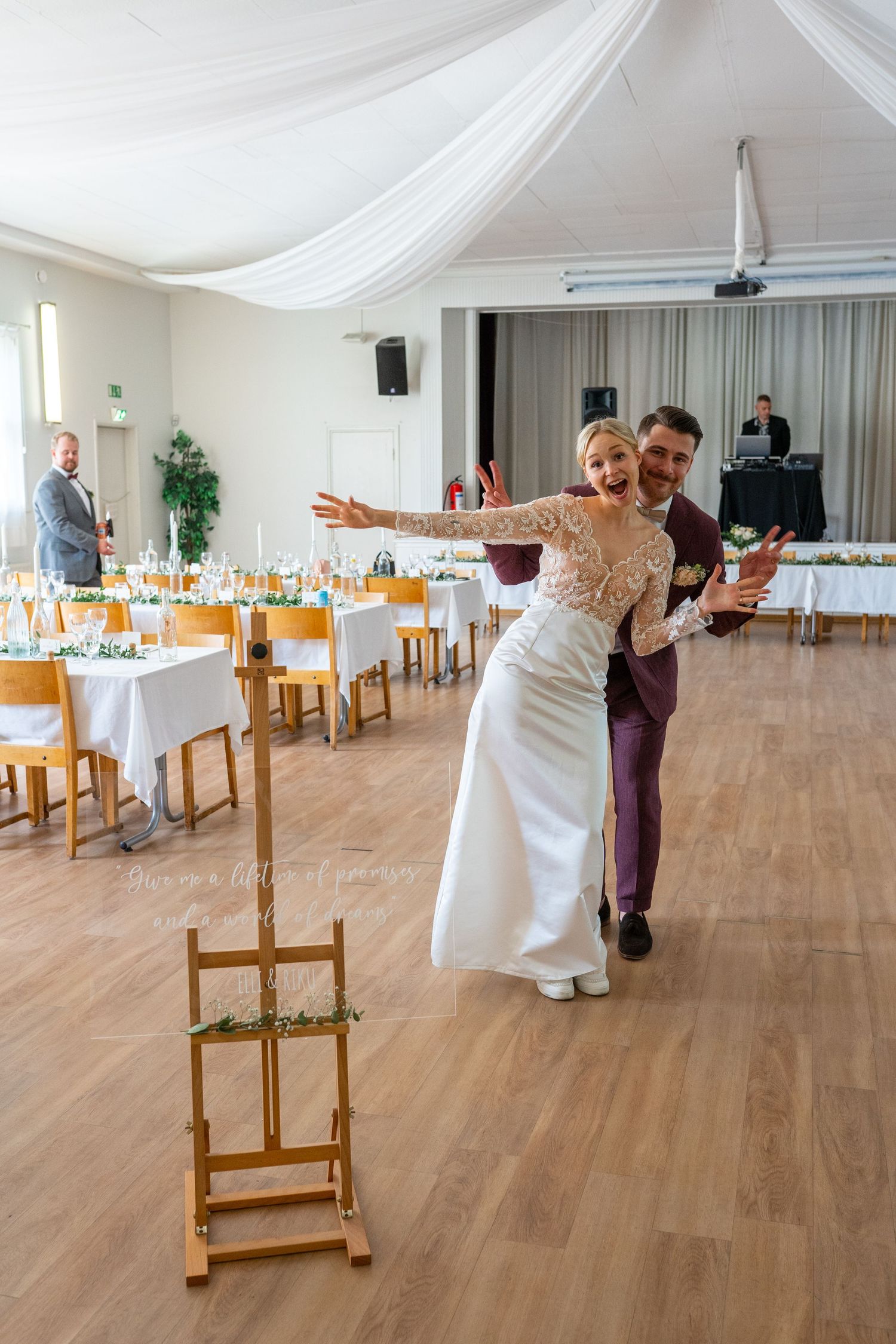 Bride and groom make joyful entrance into decorated wedding reception hall with guests and DJ.