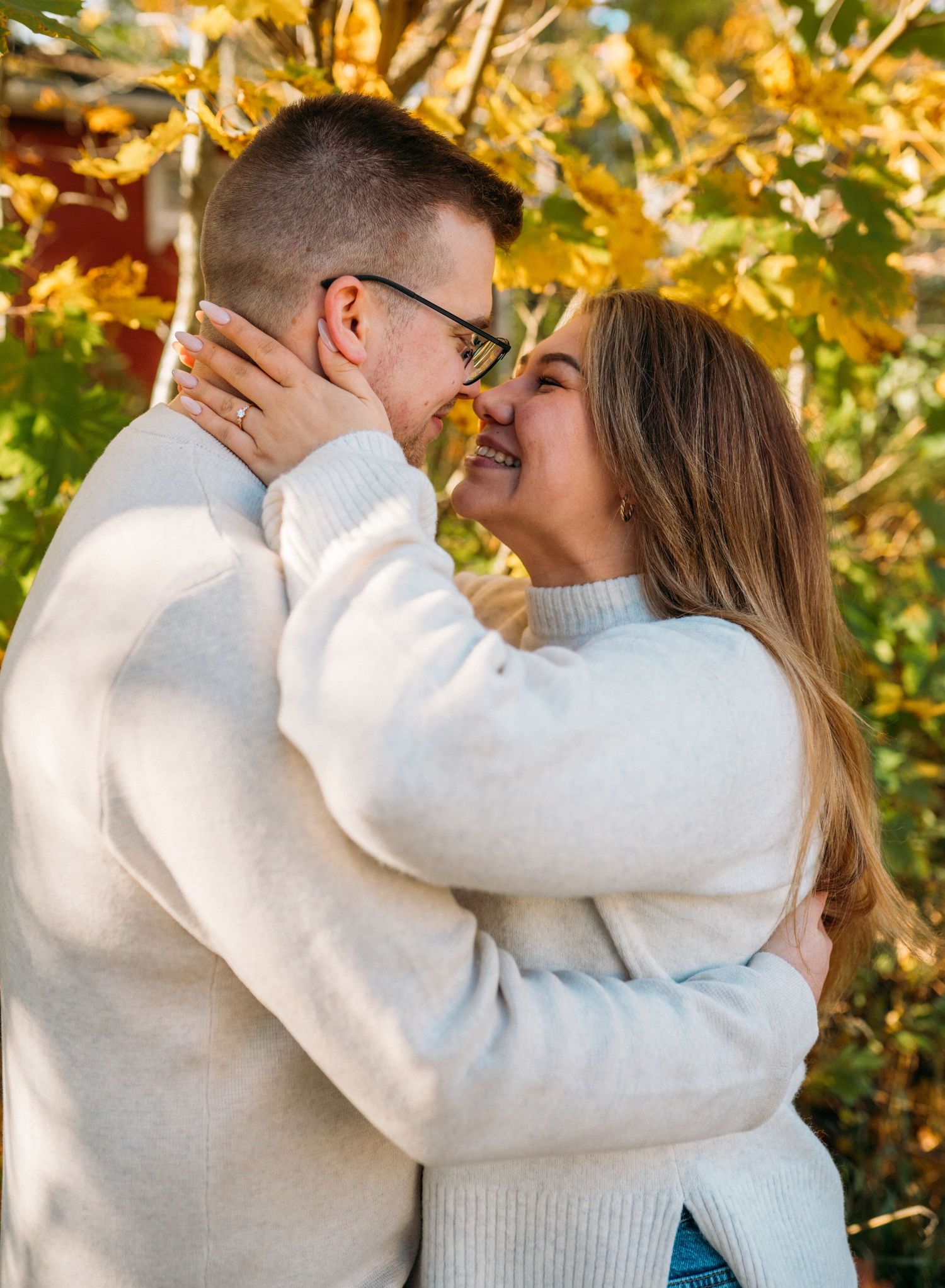 Couple in matching white sweaters sharing a romantic moment outdoors among golden autumn leaves.