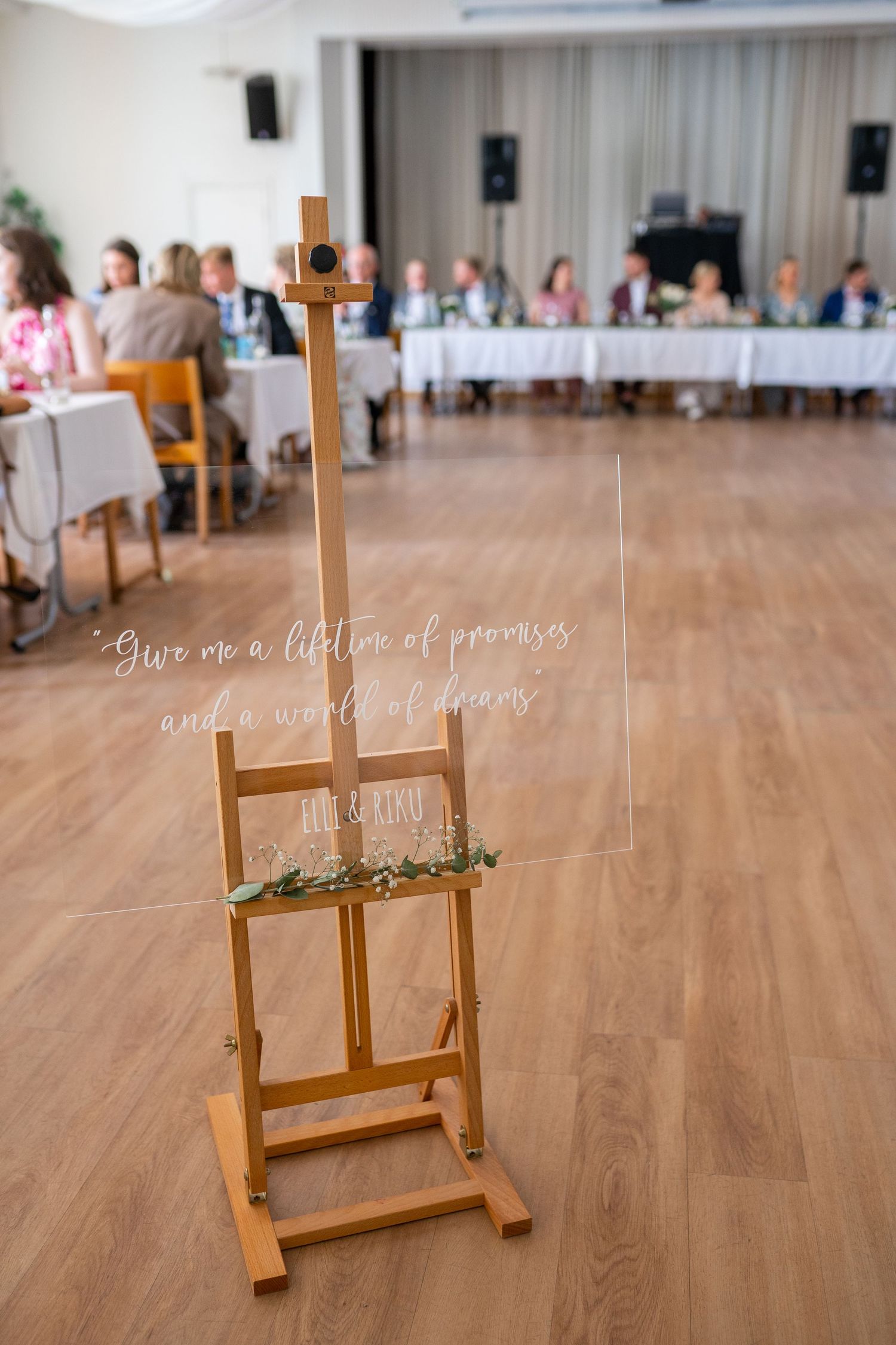 Wooden easel with a romantic quote and floral decor in a bright wedding reception hall.