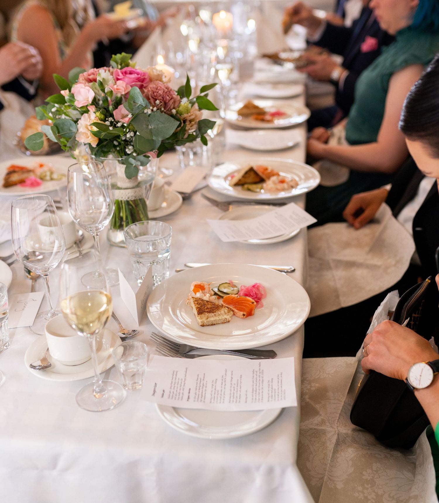 Elegant wedding reception table with white linens, pink flowers, wine glasses, and plated appetizers.