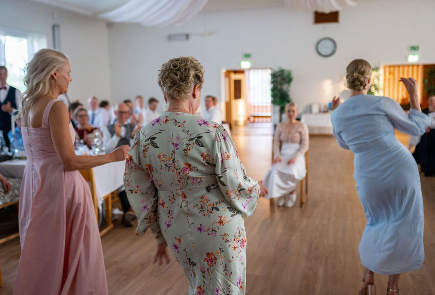 Three women in elegant dresses performing a choreographed surprise dance at wedding reception.