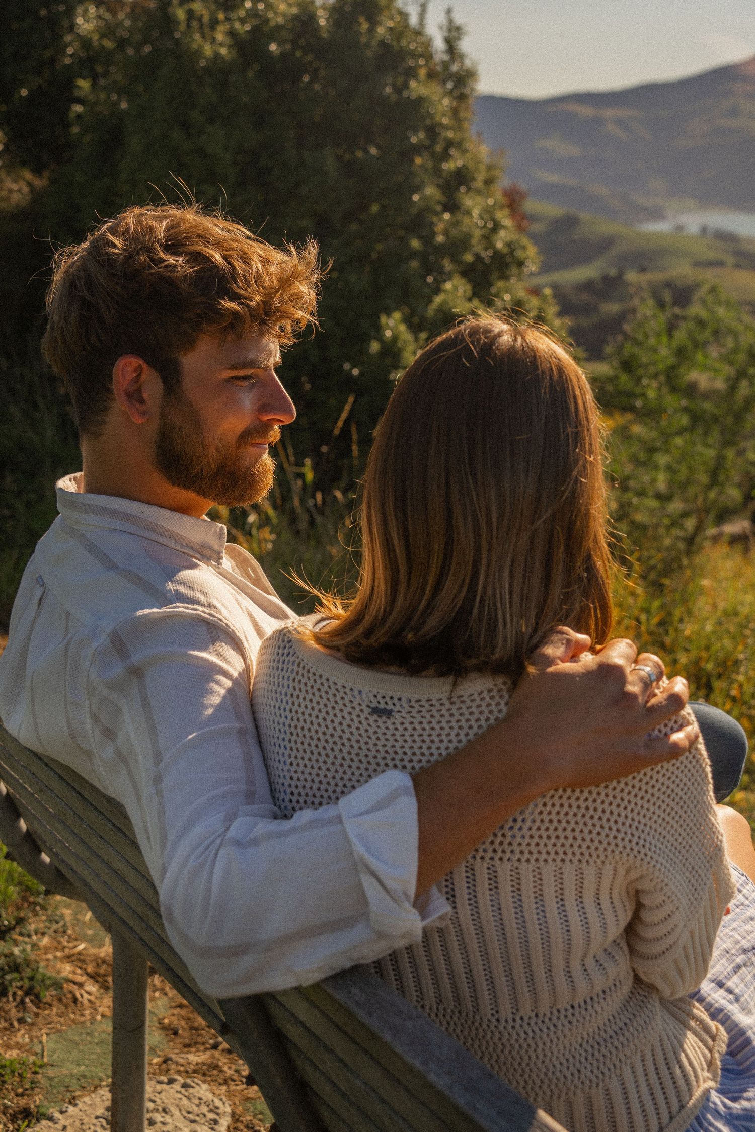 Couple sitting on a bench embracing while enjoying a scenic mountain valley view at sunset.