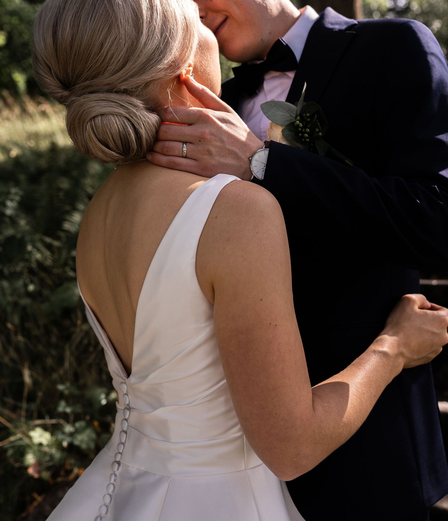 Bride and groom sharing a kiss outdoors, bride wearing elegant backless white wedding gown with chic updo hairstyle.