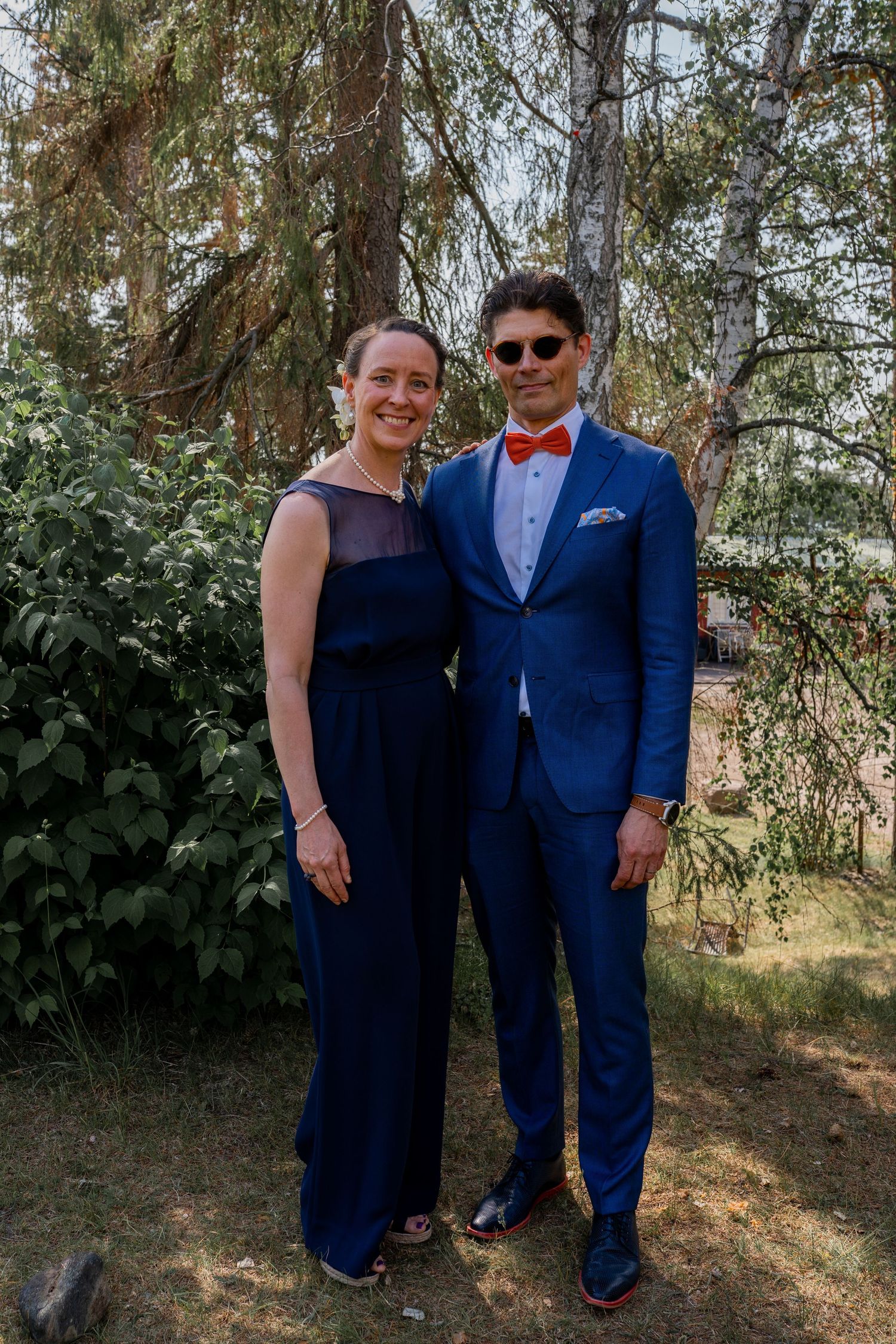 Elegant couple posing together outdoors, man in blue suit with red bow tie.