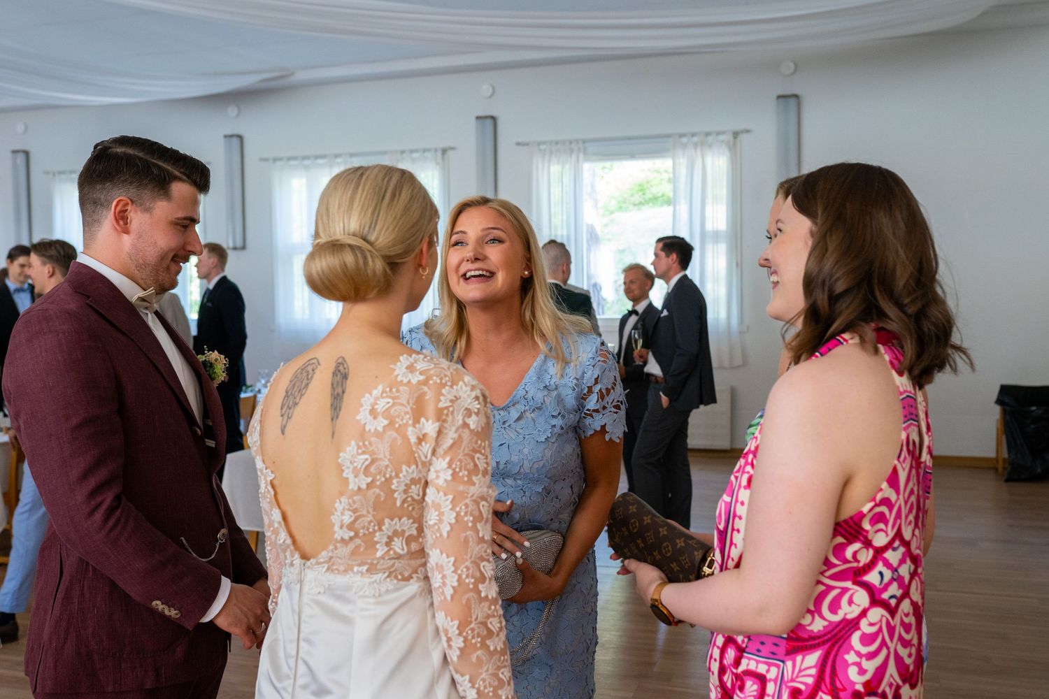 Guests laughing and conversing at a wedding reception in an elegant bright venue.