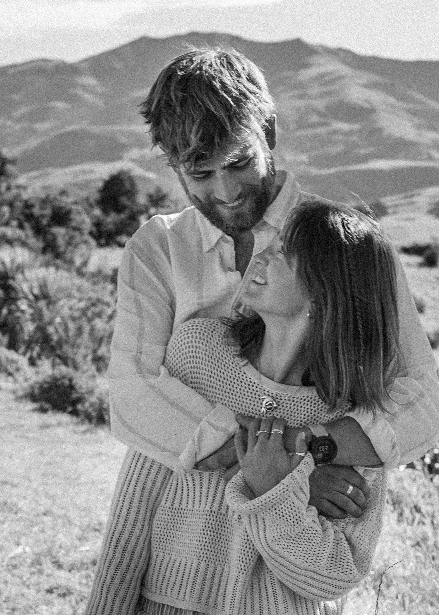 A black and white photo of a couple sharing a tender embrace with rolling hills in the background.