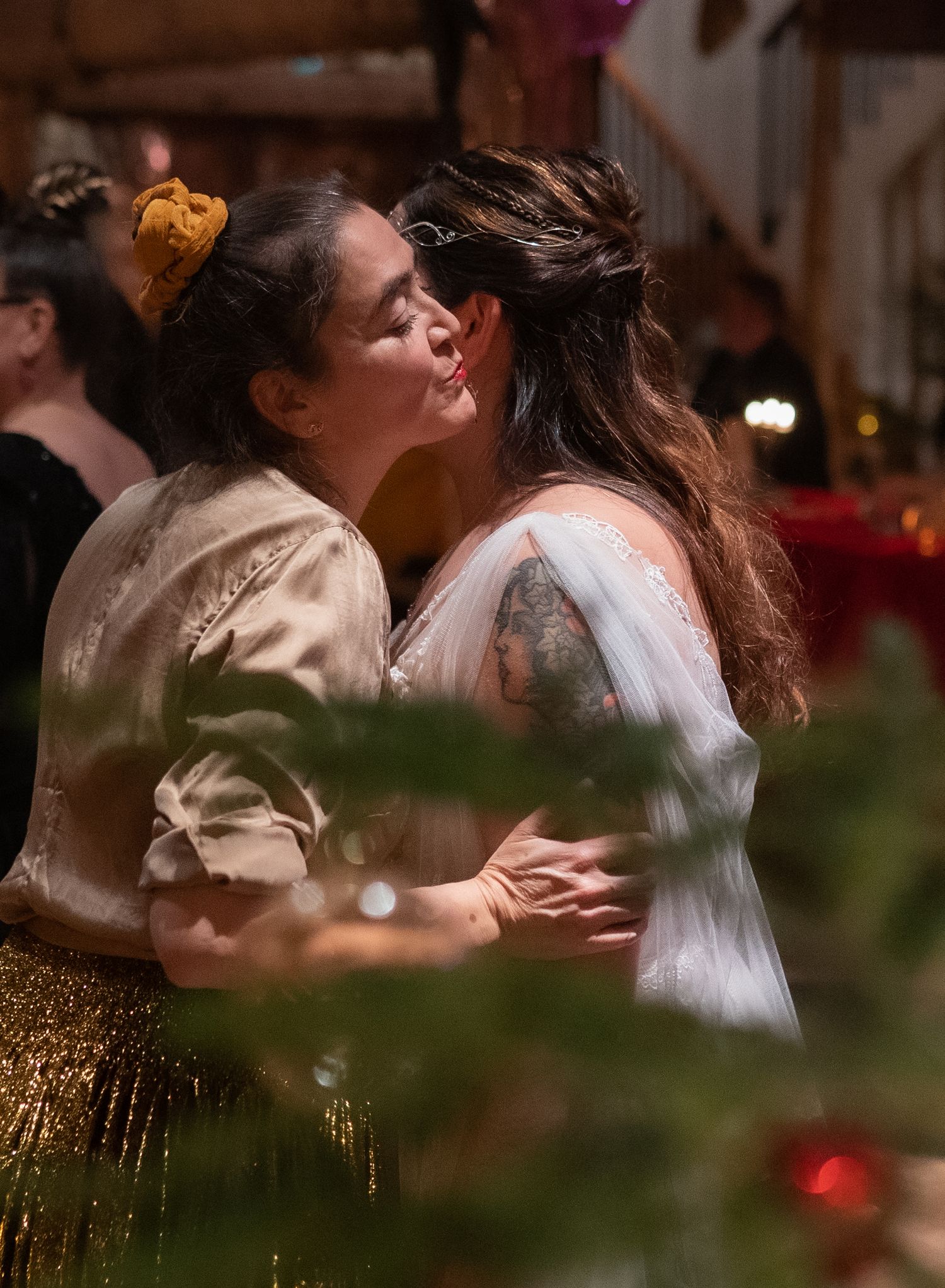 Two women sharing a kiss at a festive wedding celebration, with Christmas decorations in the foreground.