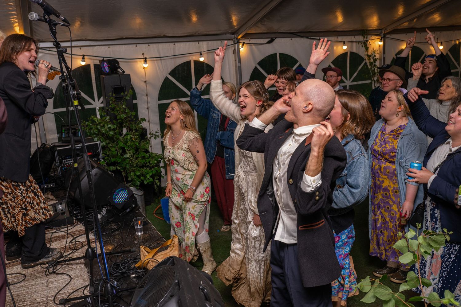 Wedding guests dance and celebrate joyfully under a tent at a lively evening reception.