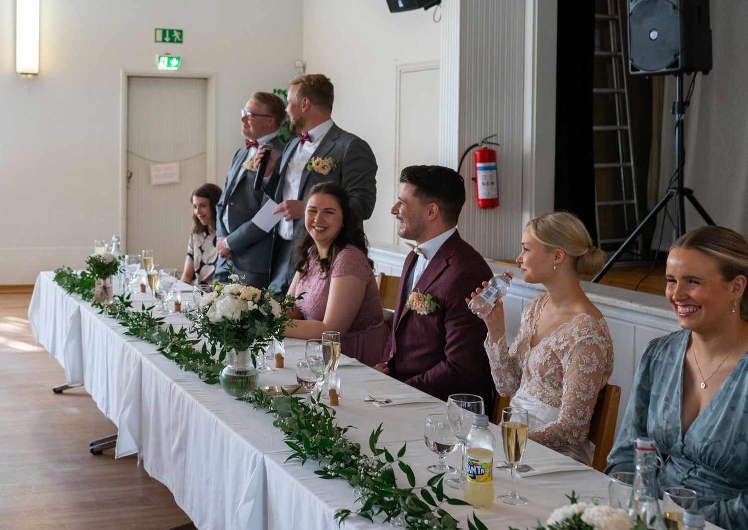 Wedding guests laughing at head table adorned with white floral garland decorations.