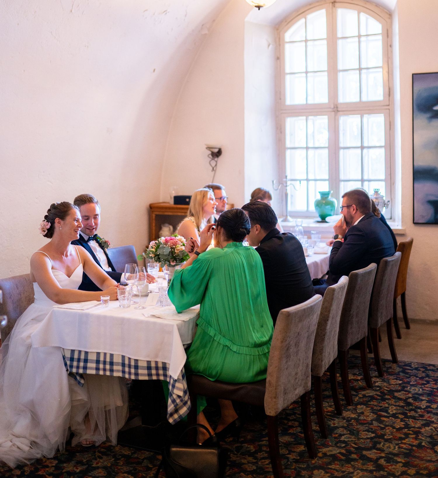 Wedding party dines at decorated table in a rustic vaulted venue.