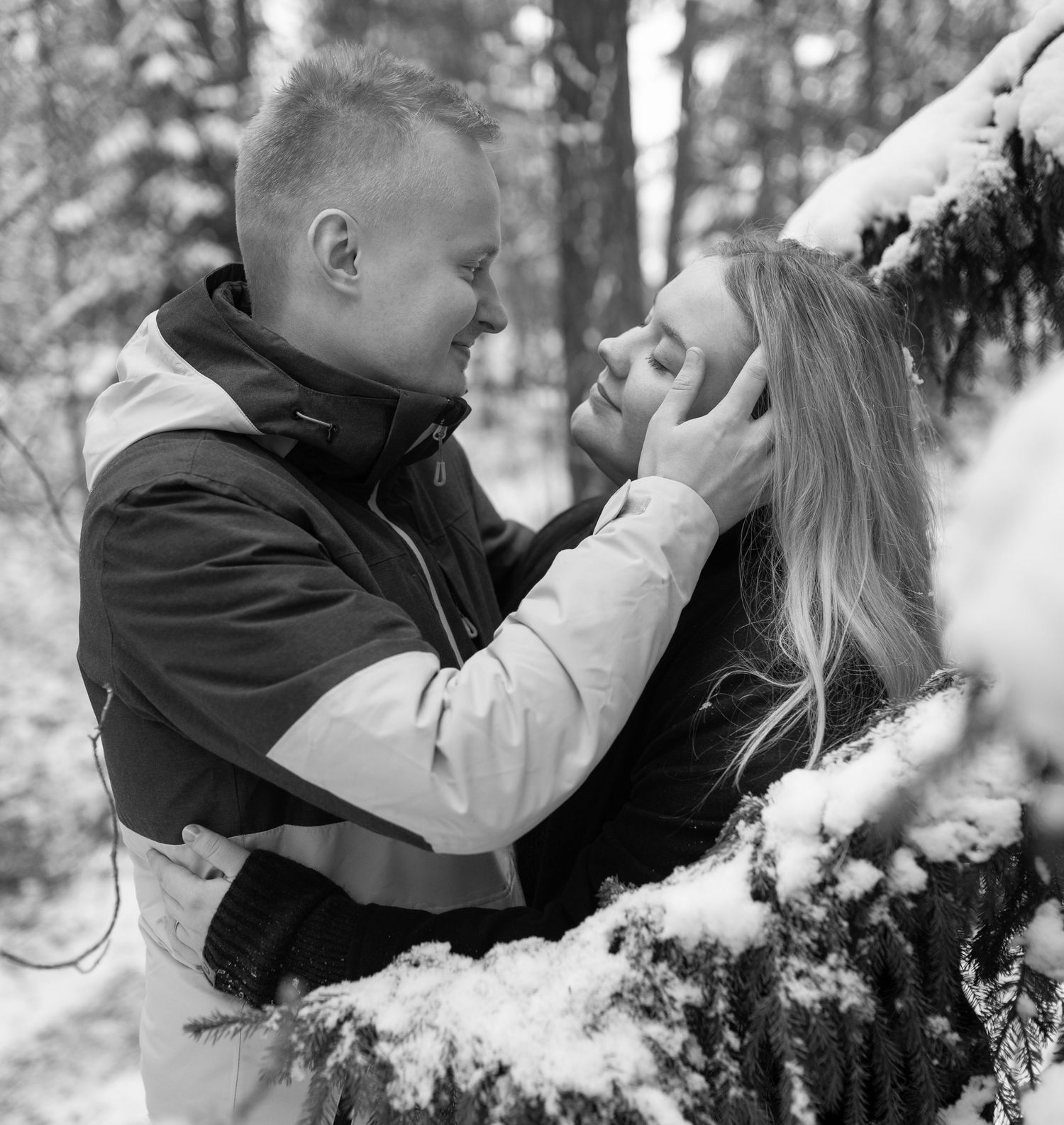 Black and white photo of romantic couple sharing tender moment in snowy winter forest.