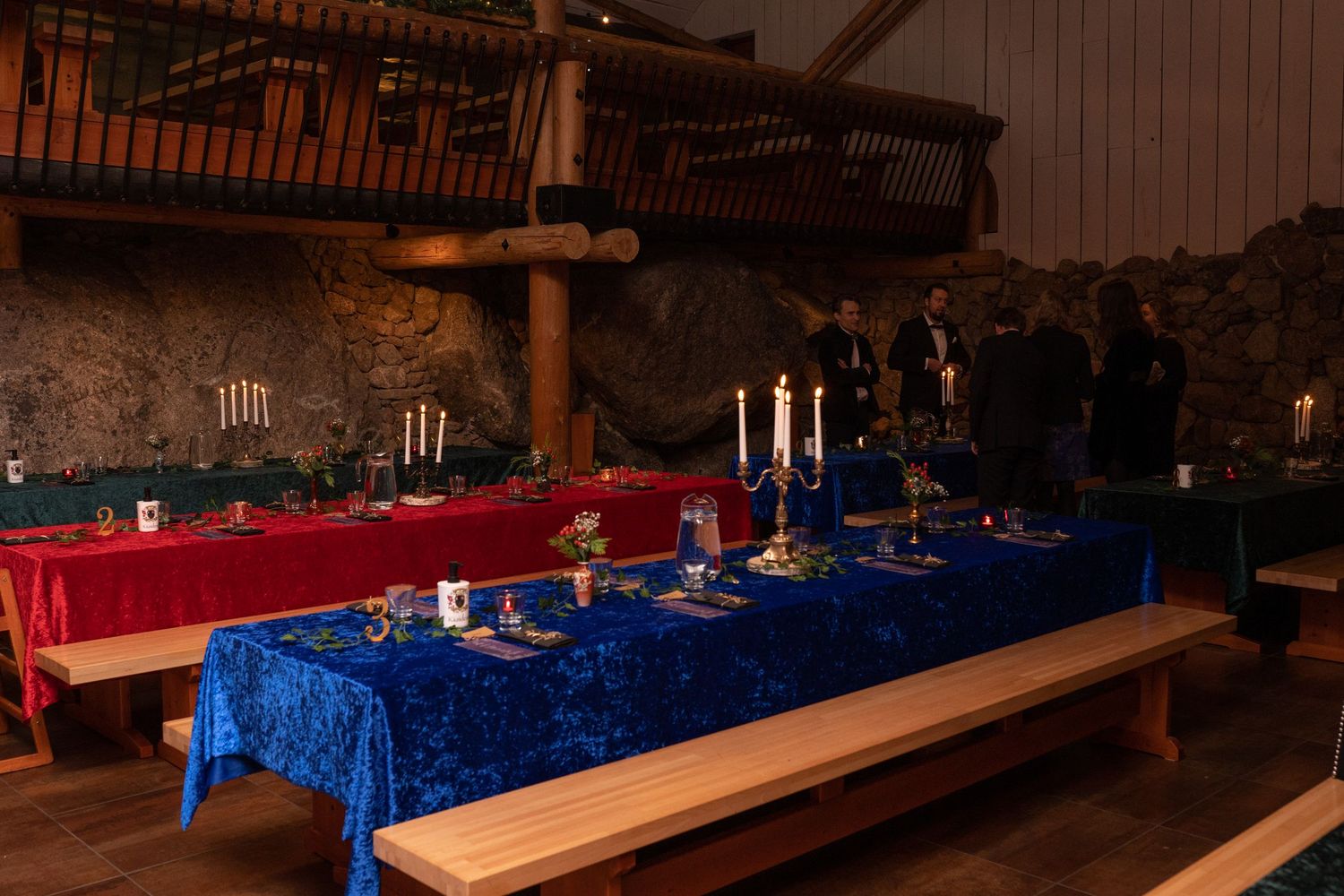 Elegant medieval banquet hall with blue and red velvet tablecloths, candelabras, and rustic stone walls.