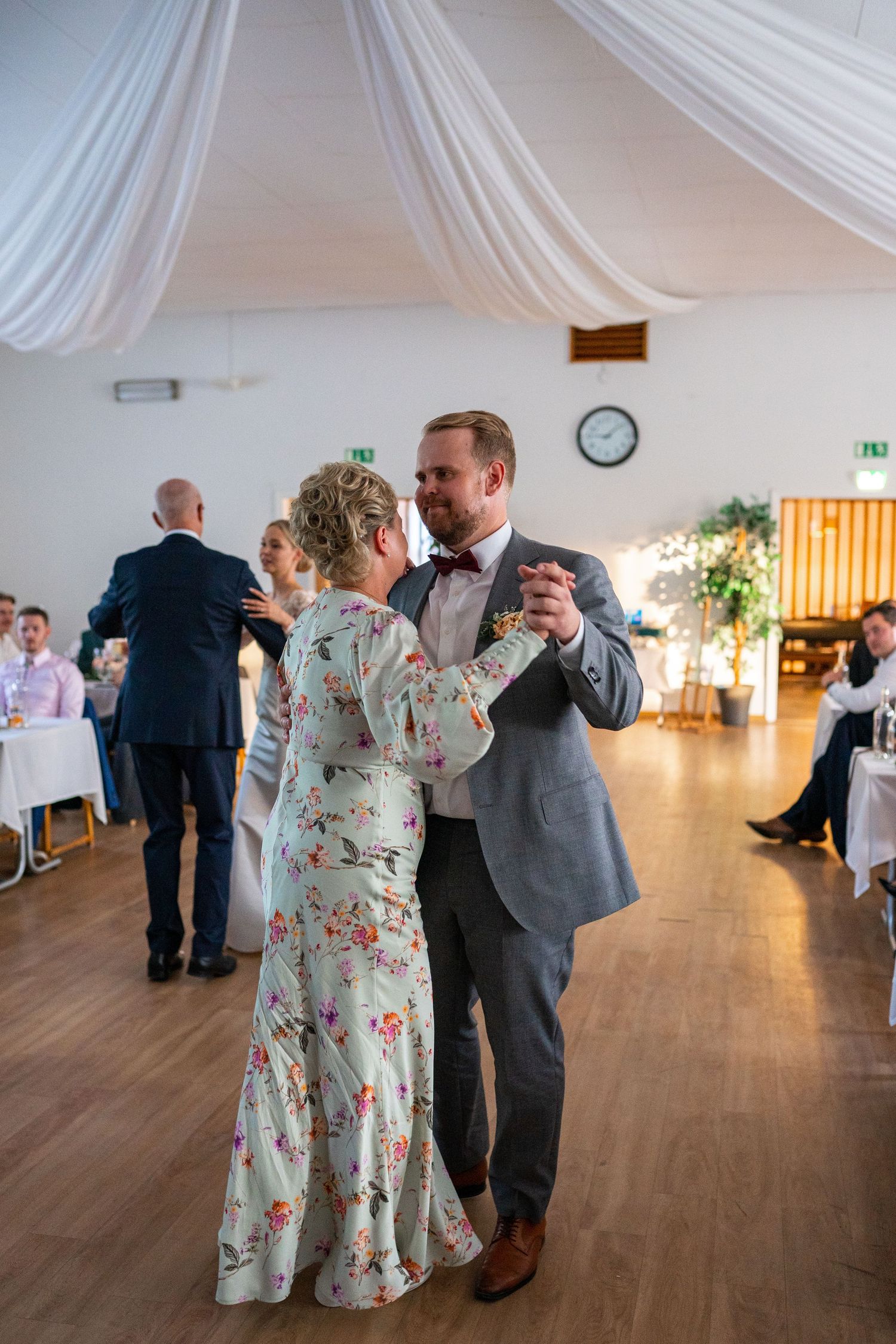 Couple sharing a romantic first dance at wedding reception in decorated hall with draped ceiling.