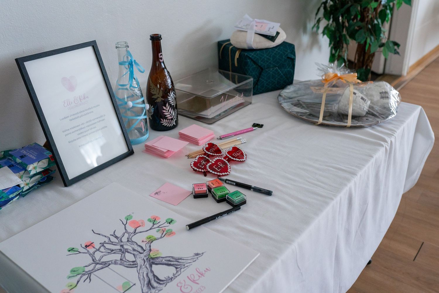Wedding gift table with a guest book tree, heart decorations, champagne bottle, and framed certificate.