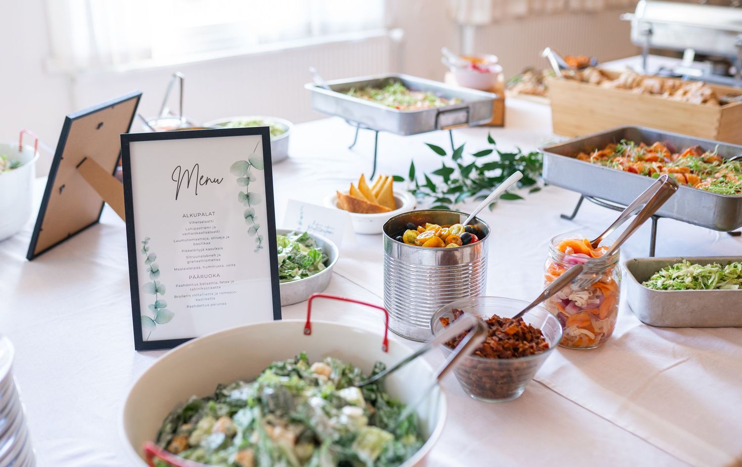 Elegant wedding buffet table with fresh salads, colorful dishes, and a menu sign at a reception.