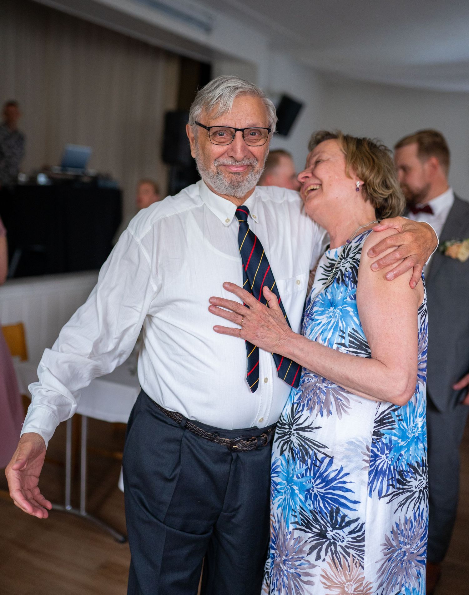 Elderly couple sharing a joyful dance at wedding reception, man in white shirt and striped tie.