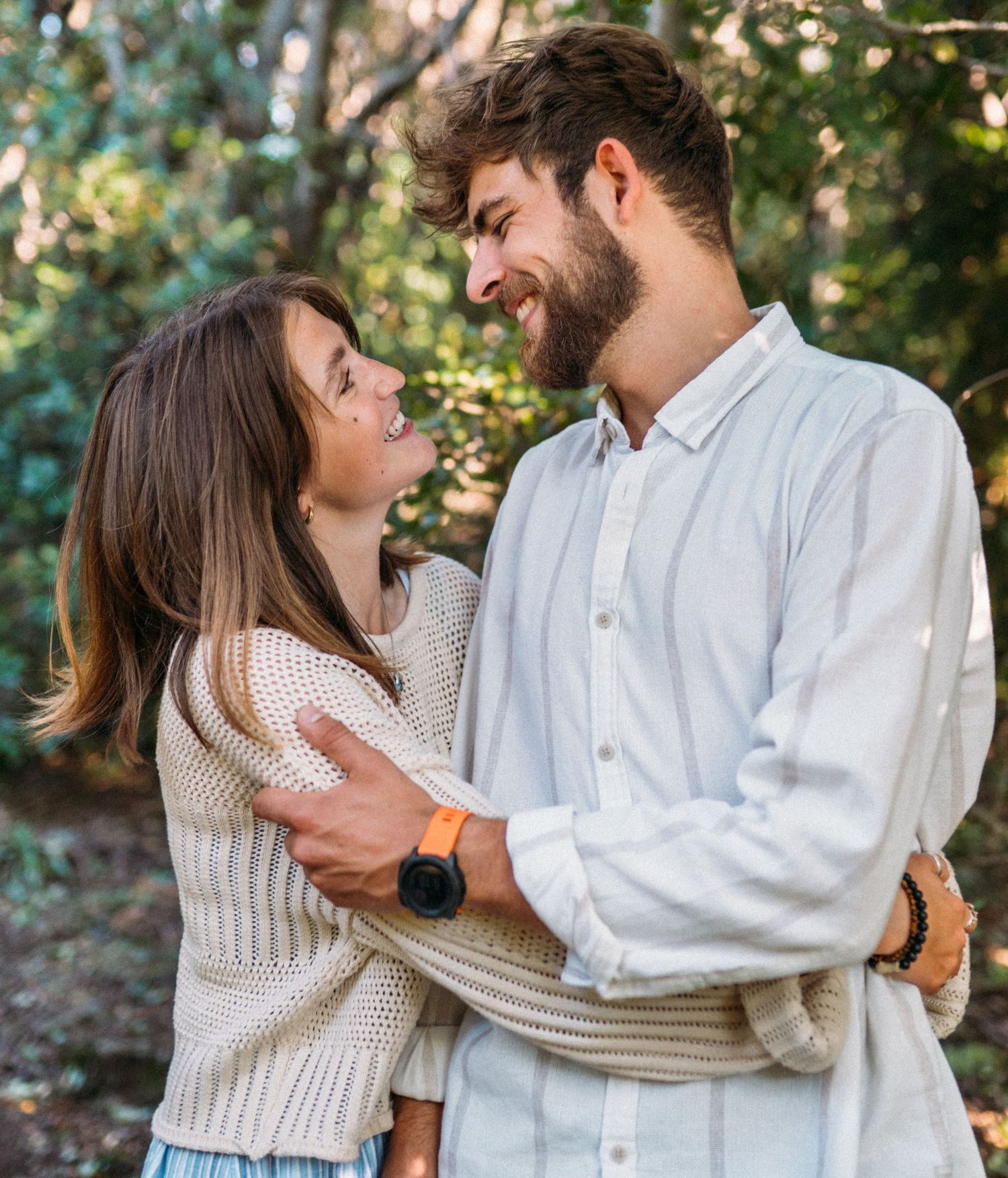 Smiling couple embracing outdoors in a lush green park, gazing lovingly at each other.