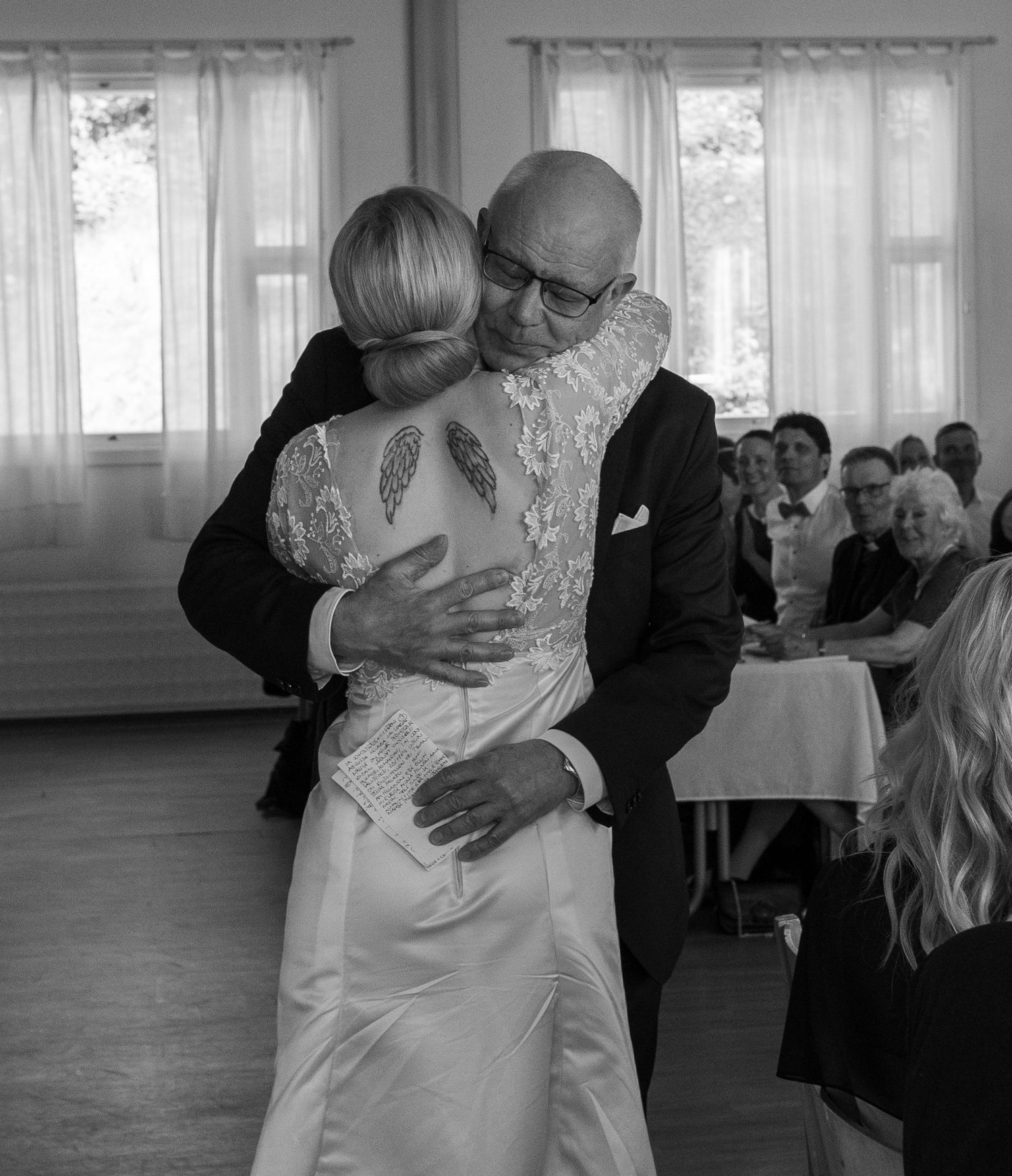 Black and white photo of a bride and bald groom sharing an emotional hug during their wedding reception.