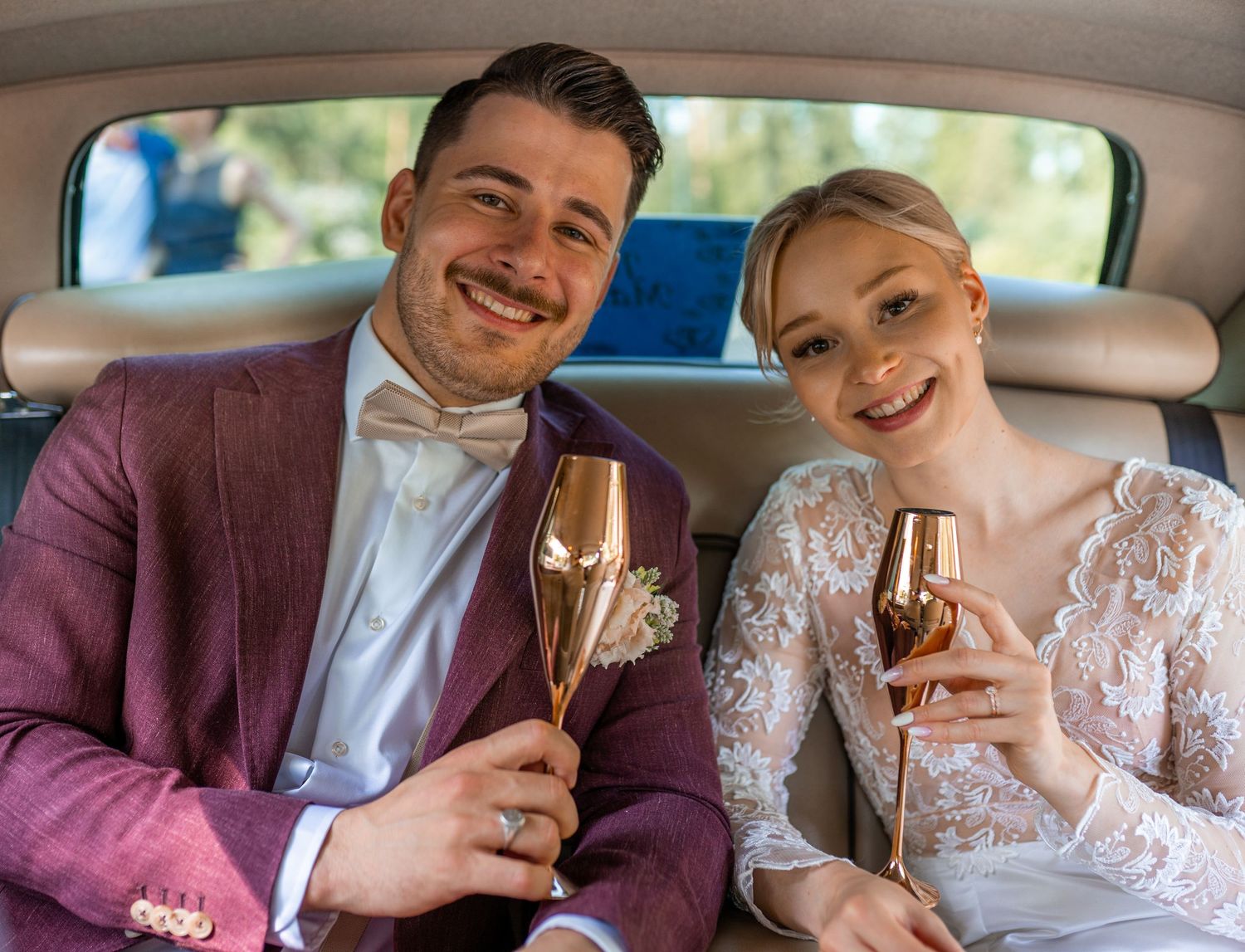Bride and groom toasting with gold champagne flutes in the backseat of a wedding car.