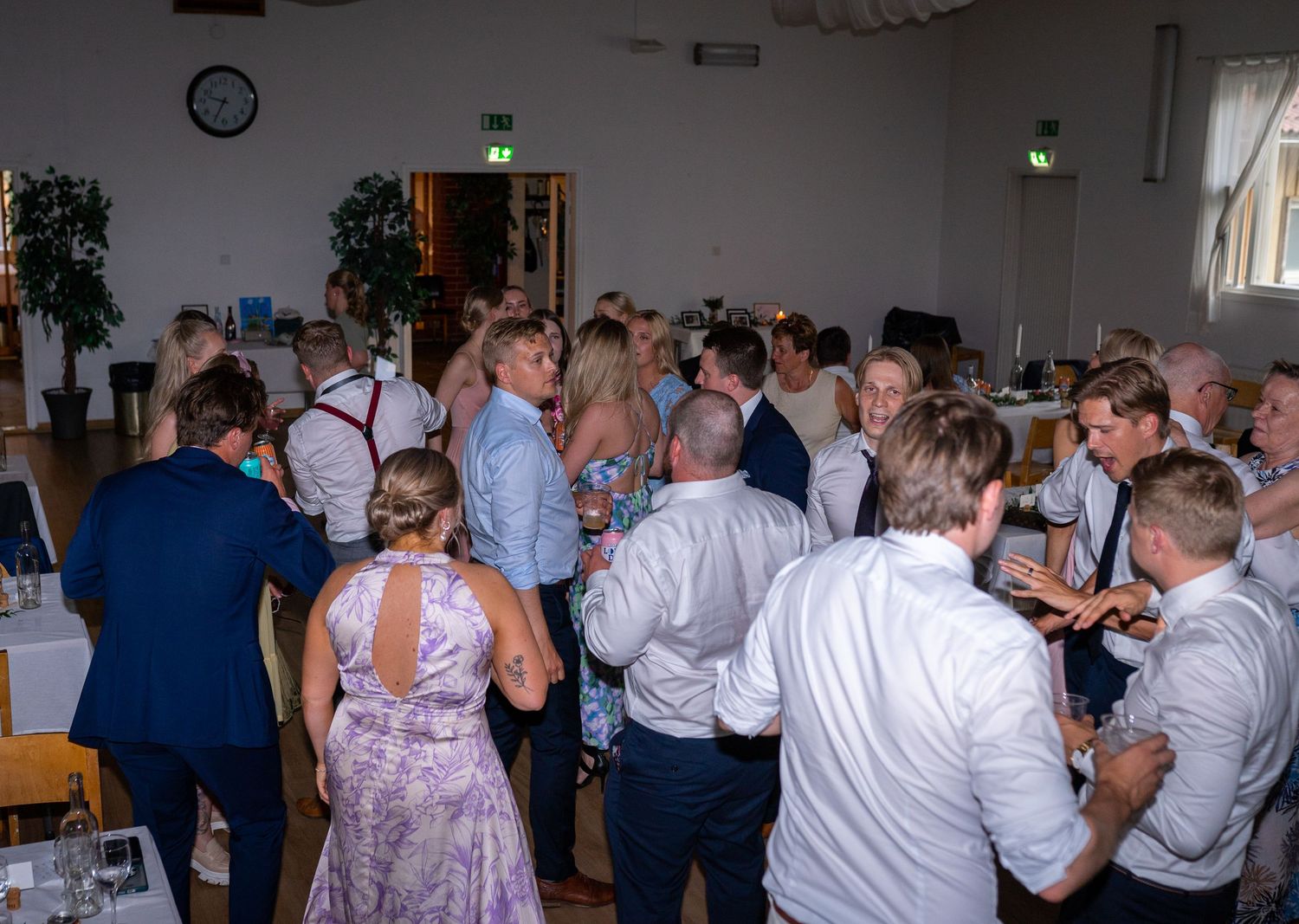 Large crowd of wedding guests socializing and dancing together in a decorated reception banquet hall.