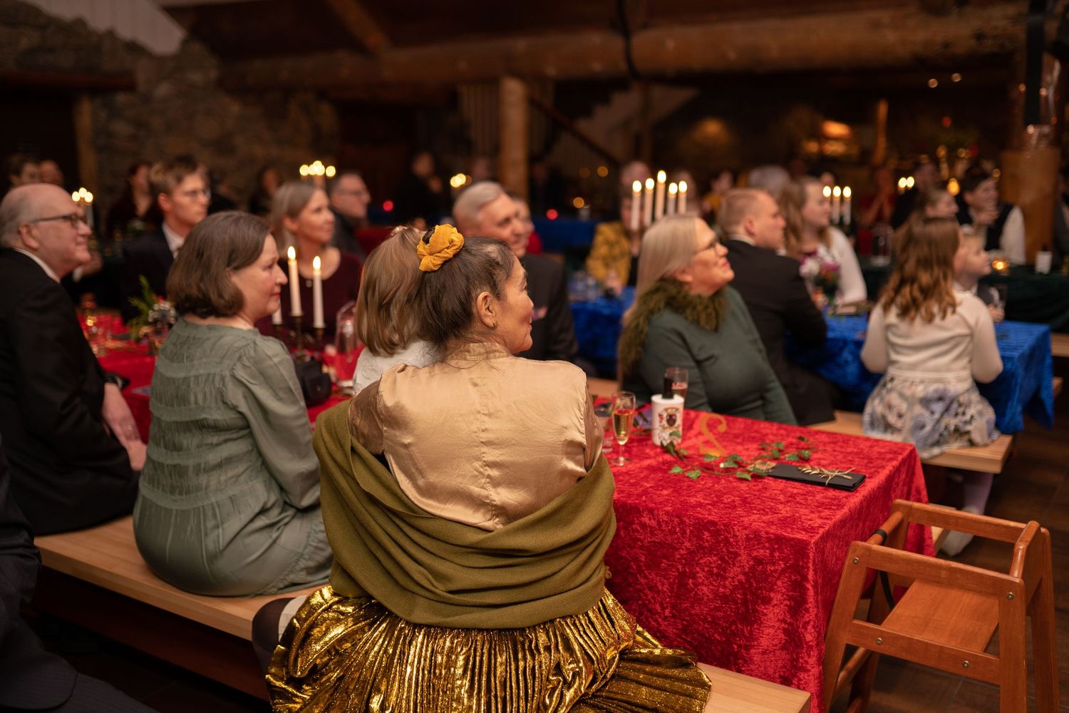 Guests in elegant attire seated on wooden benches at a candlelit medieval banquet hall event.
